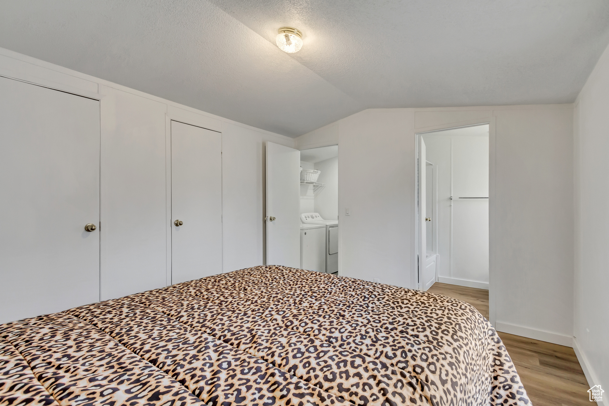 Bedroom featuring light wood-type flooring, ensuite bathroom, vaulted ceiling, and washing machine and clothes dryer