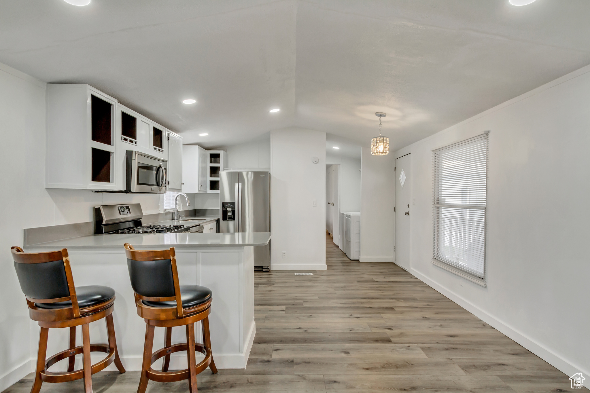 Kitchen with kitchen peninsula, appliances with stainless steel finishes, decorative light fixtures, white cabinets, and light wood-type flooring