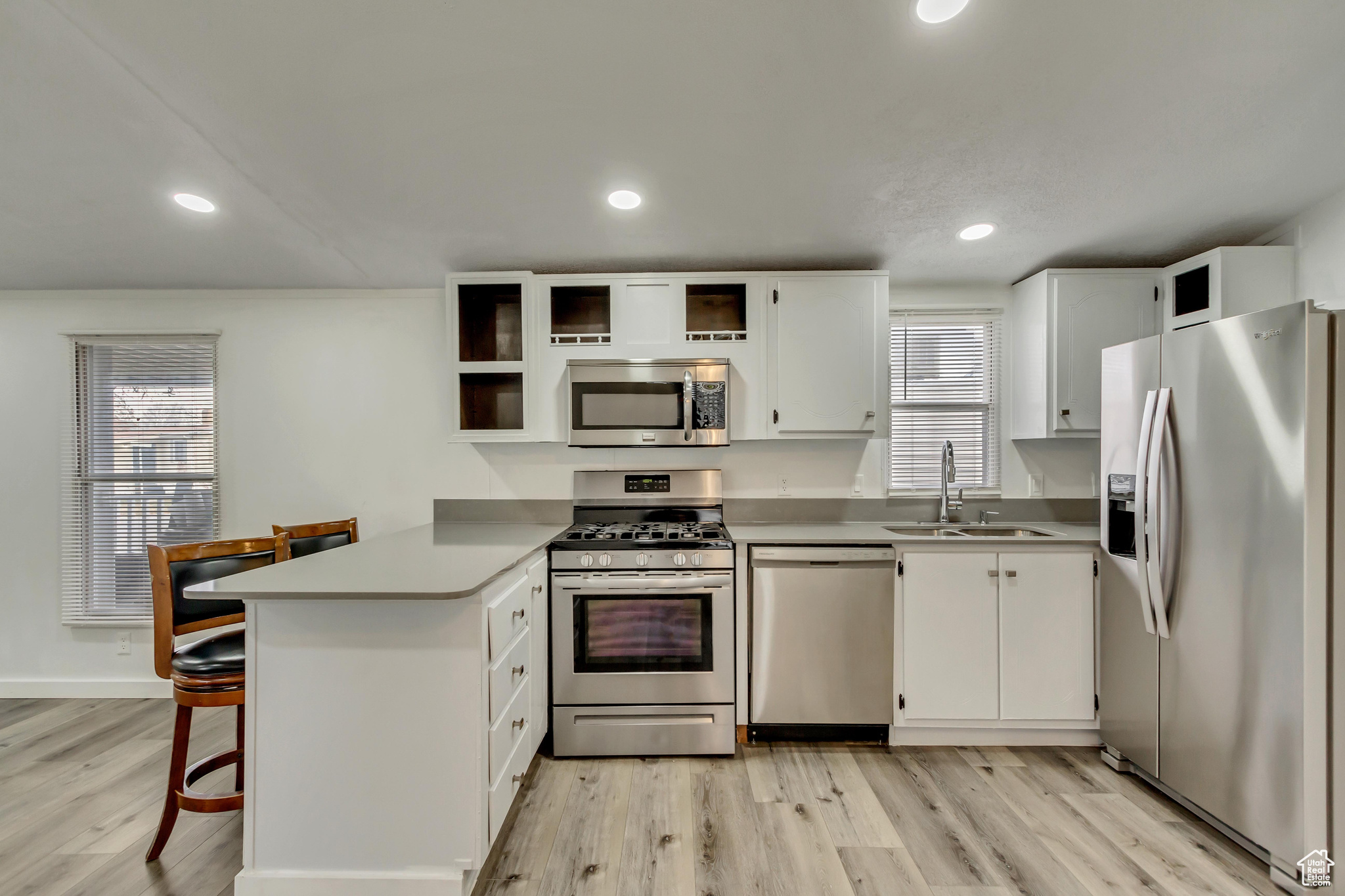 Kitchen with kitchen peninsula, light wood-type flooring, stainless steel appliances, sink, and white cabinets