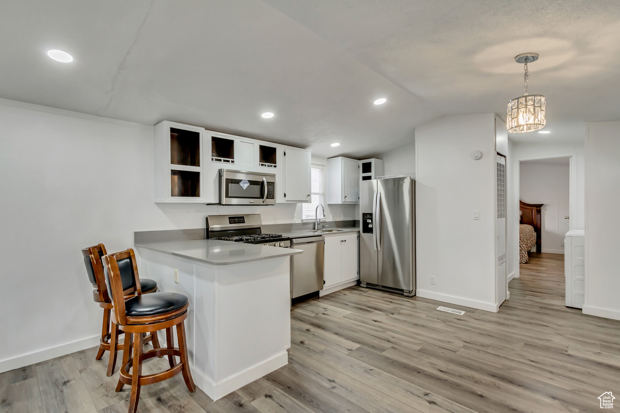 Kitchen with light wood-type flooring, decorative light fixtures, white cabinetry, kitchen peninsula, and stainless steel appliances