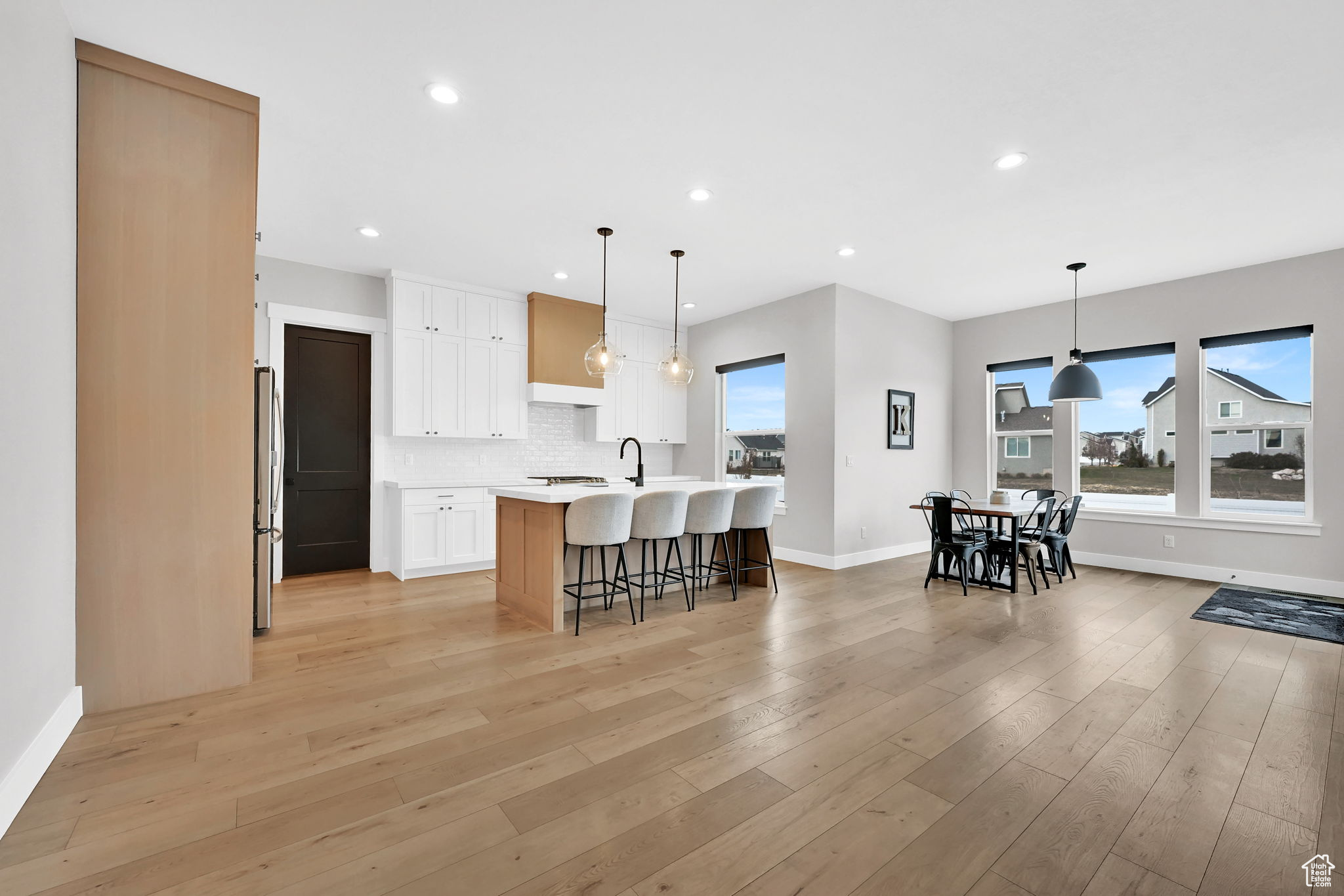 Kitchen featuring light wood-type flooring, a breakfast bar, pendant lighting, white cabinetry, and an island with sink