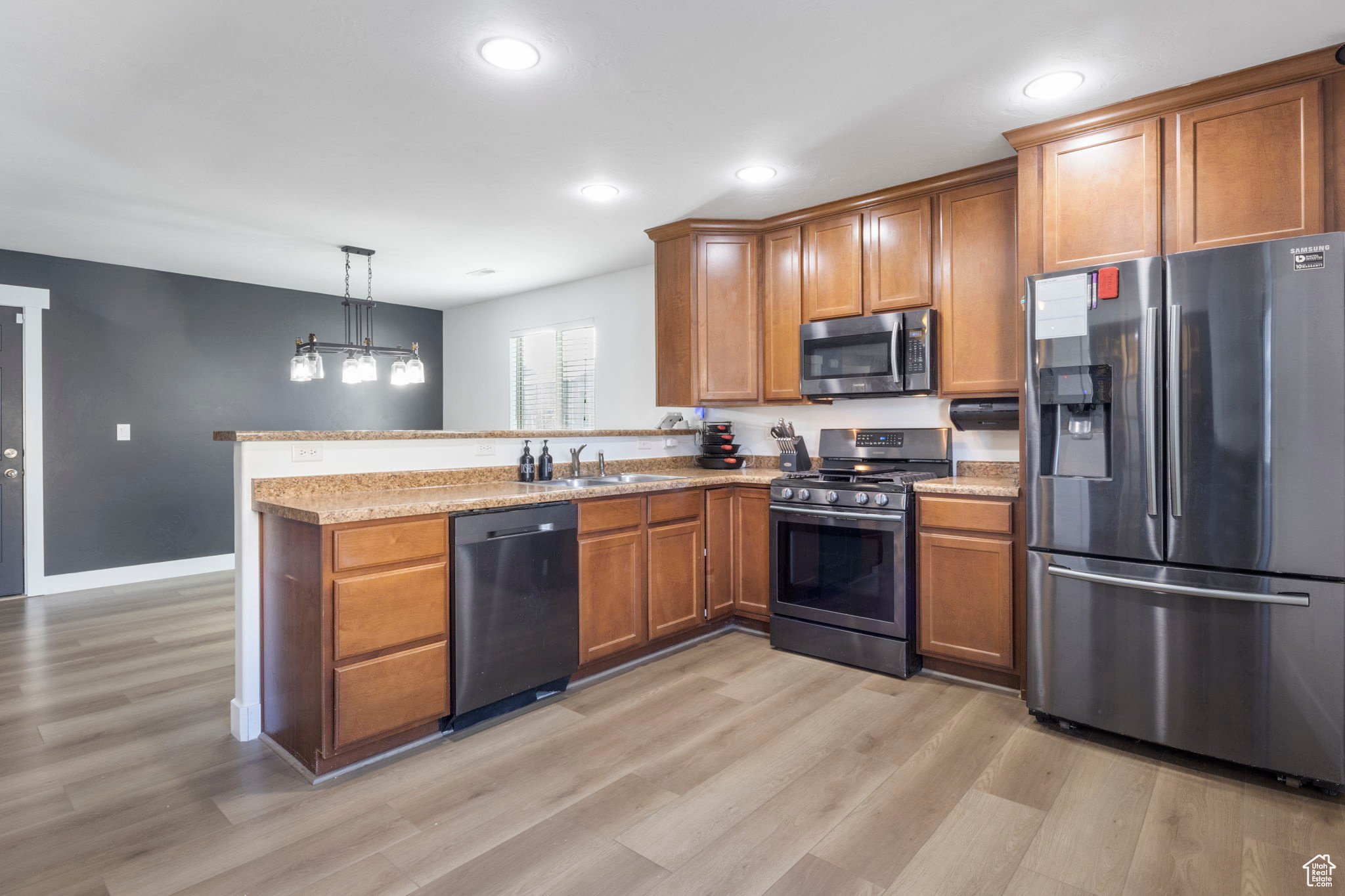 Kitchen featuring sink, stainless steel appliances, kitchen peninsula, pendant lighting, and light wood-type flooring