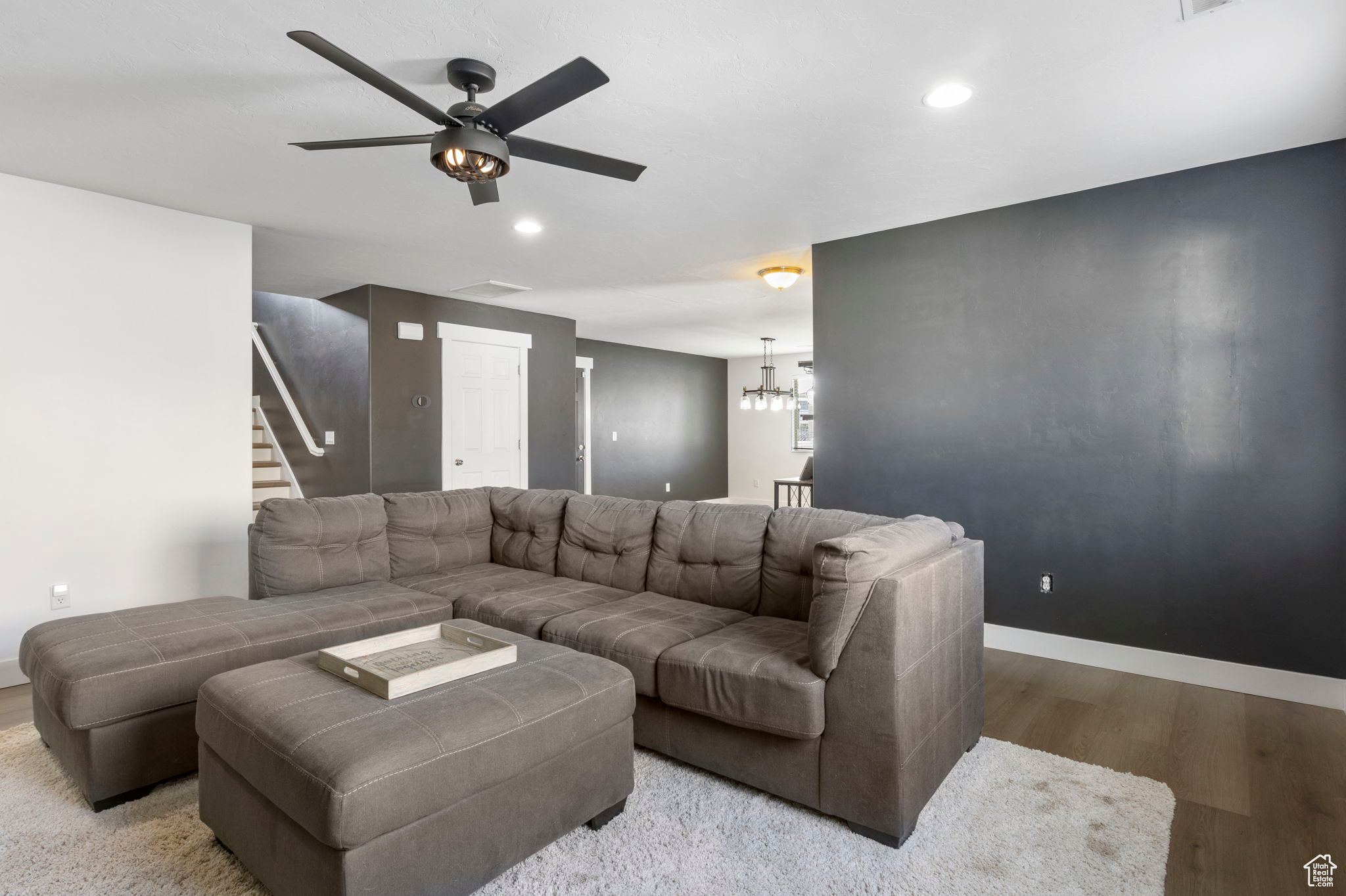 Living room with ceiling fan with notable chandelier and light wood-type flooring