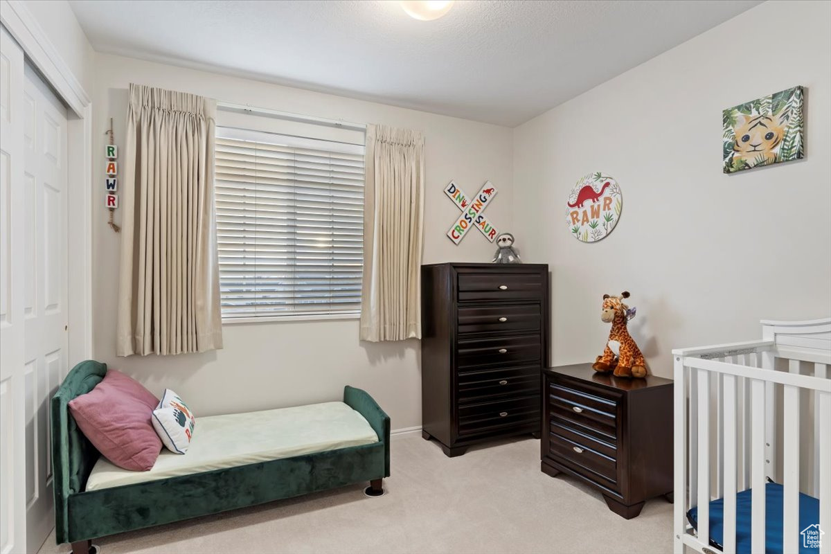 Bedroom with a nursery area, light carpet, and a closet