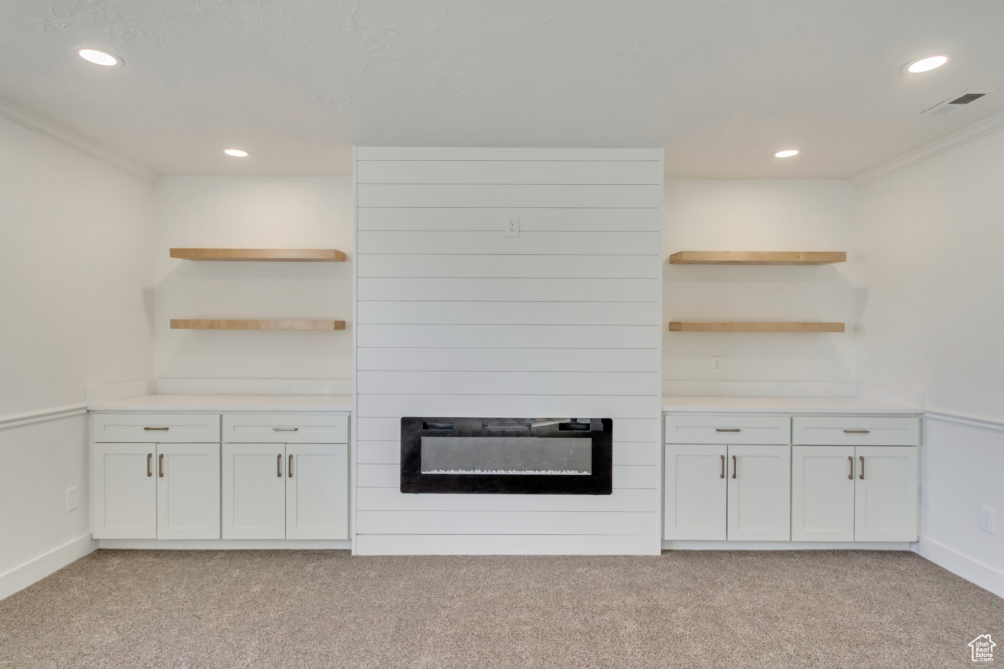 Kitchen with crown molding, white cabinets, light carpet, and a large fireplace