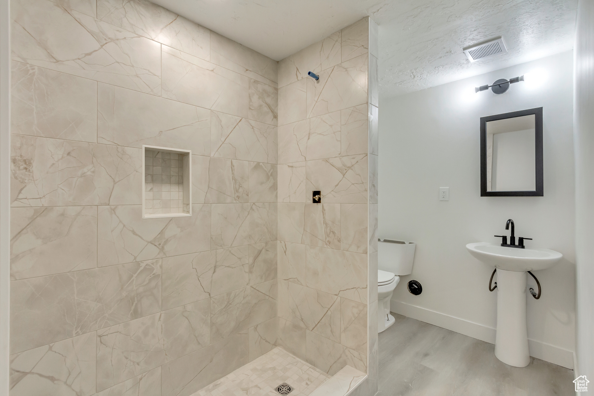 Bathroom featuring toilet, a textured ceiling, tiled shower, and hardwood / wood-style flooring