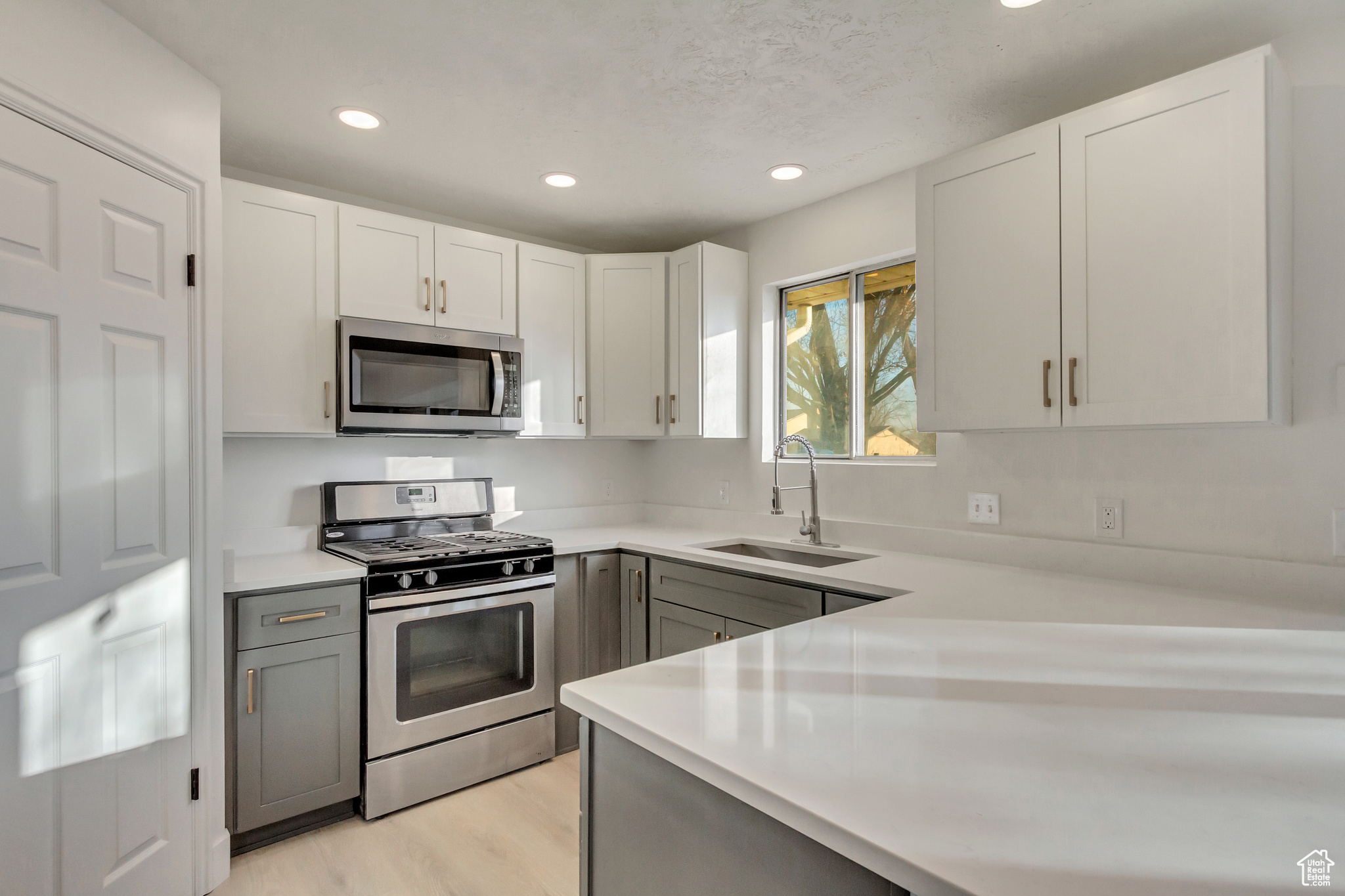 Kitchen featuring gray cabinets, stainless steel appliances, light wood-type flooring, white cabinets, and sink