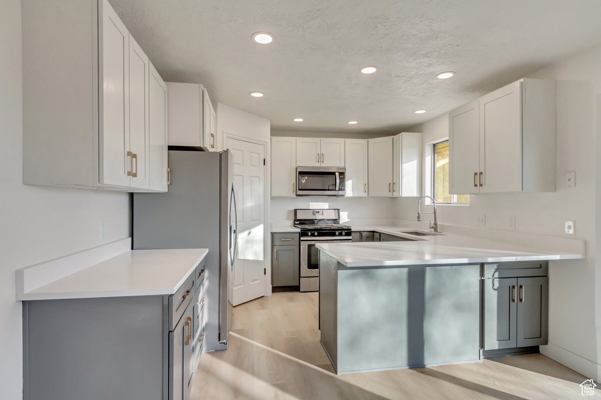 Kitchen with white cabinets, stainless steel appliances, sink, kitchen peninsula, and light hardwood / wood-style flooring