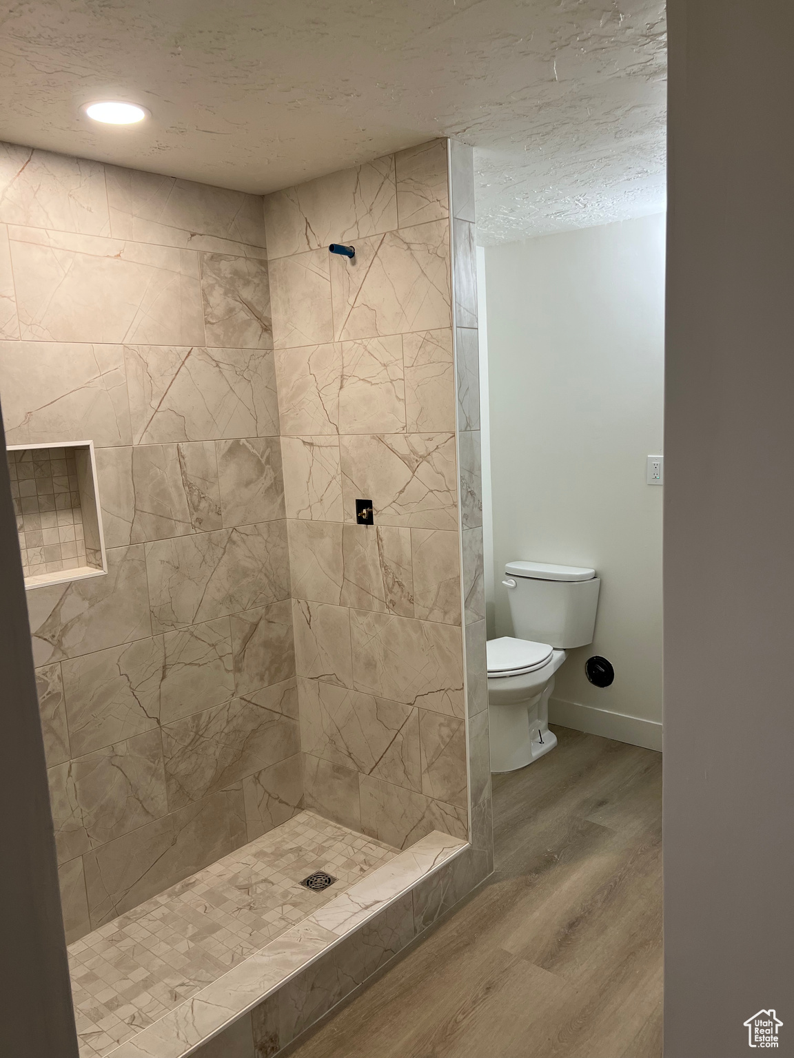 Bathroom with hardwood / wood-style flooring, a textured ceiling, toilet, and tiled shower