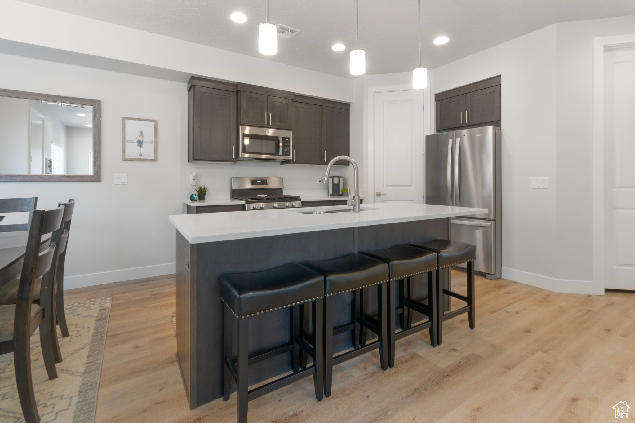 Kitchen featuring sink, an island with sink, light hardwood / wood-style floors, dark brown cabinetry, and stainless steel appliances