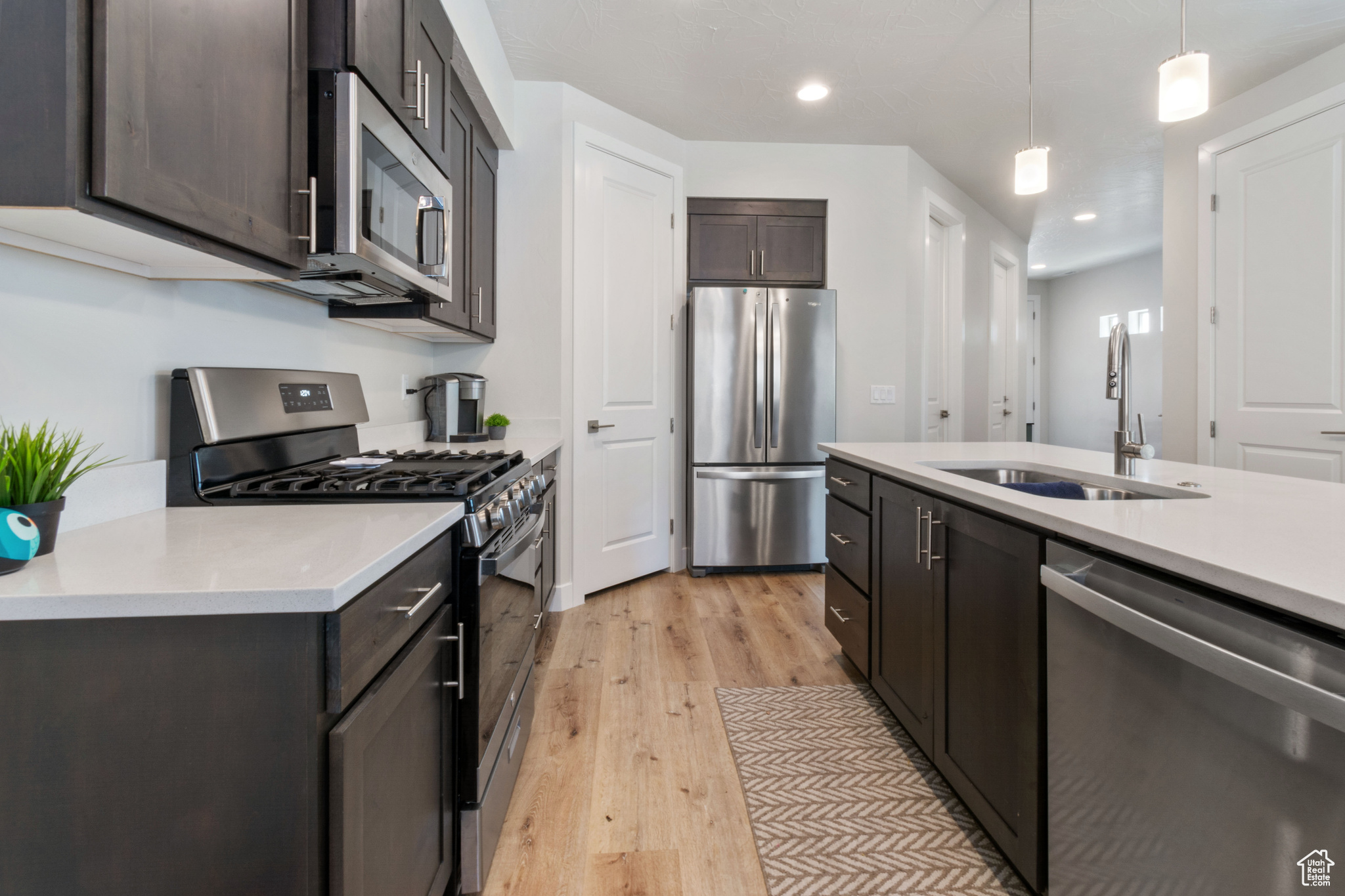 Kitchen featuring appliances with stainless steel finishes, dark brown cabinetry, sink, pendant lighting, and light hardwood / wood-style flooring