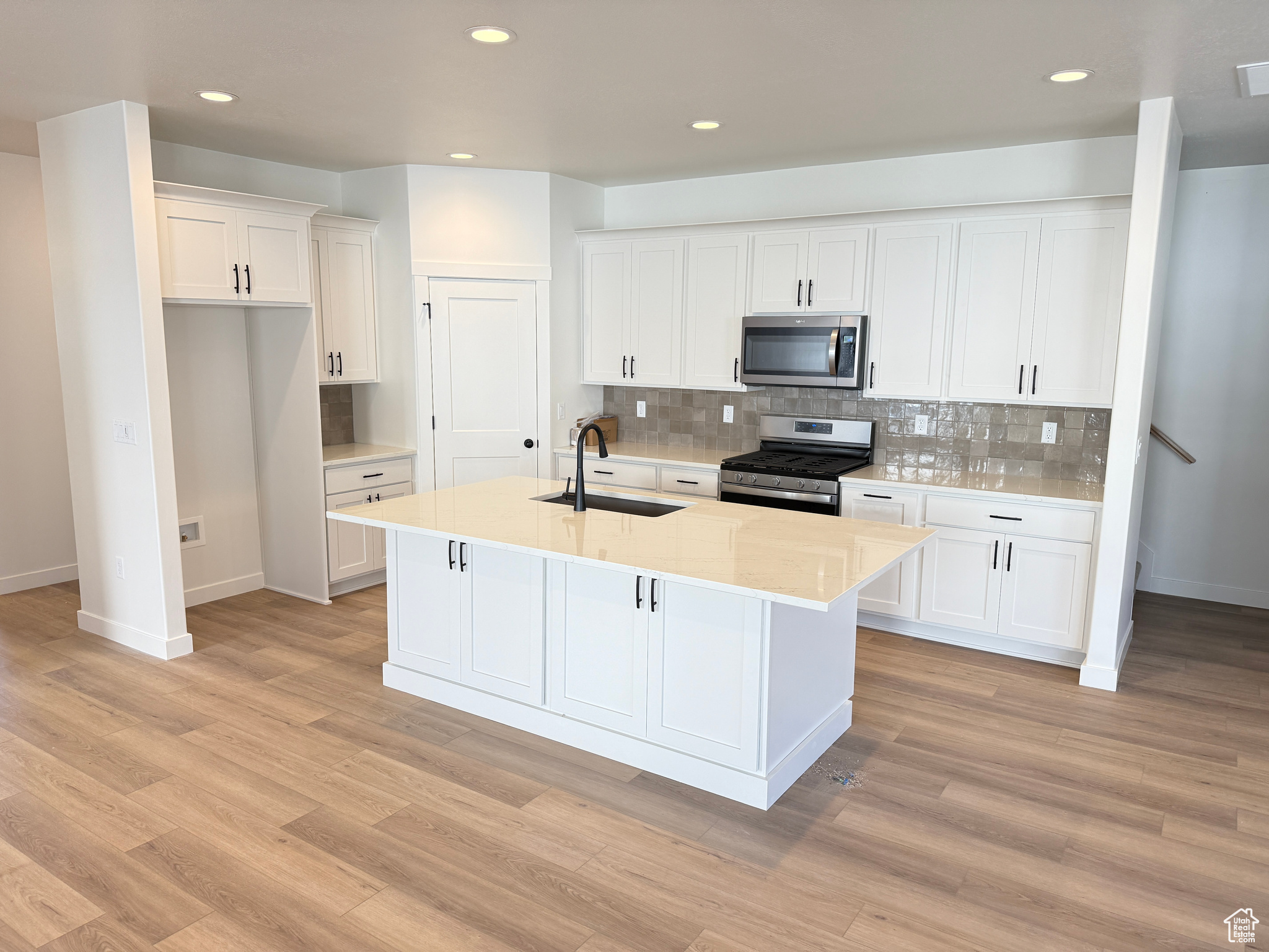 Kitchen with a kitchen island with sink, sink, white cabinets, and stainless steel appliances