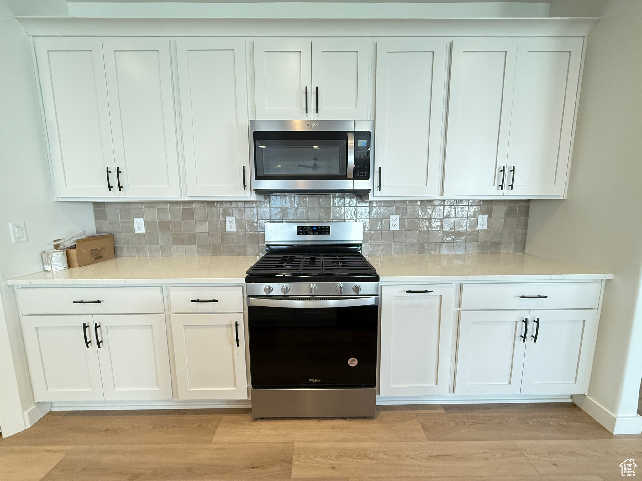 Kitchen with backsplash, light hardwood / wood-style flooring, white cabinets, and appliances with stainless steel finishes