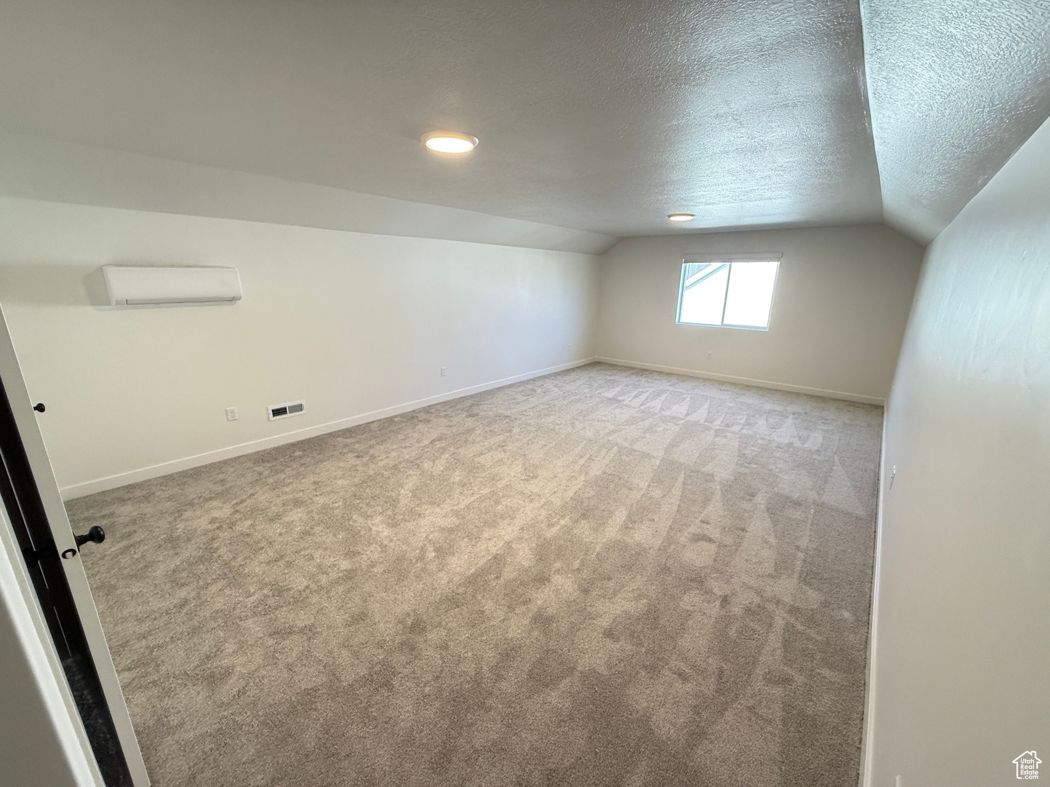 Interior space with a wall mounted AC, light colored carpet, and vaulted ceiling