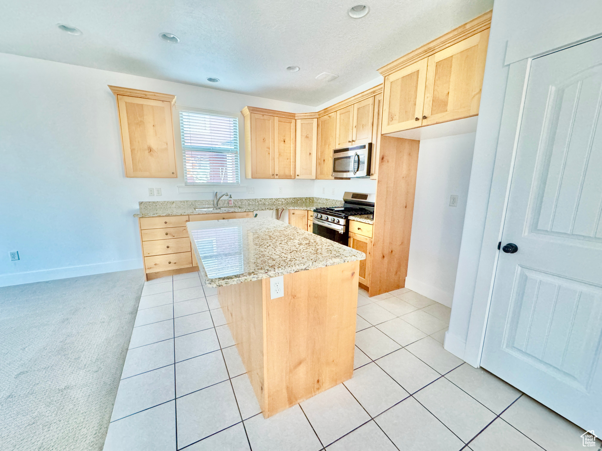 Kitchen with light brown cabinets, light tile patterned floors, a kitchen island, light stone counters, and stainless steel appliances