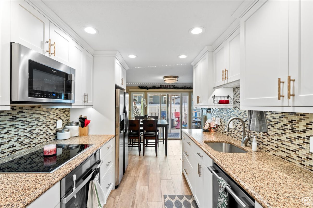 Kitchen with white cabinets, stainless steel appliances, light stone counters, and sink