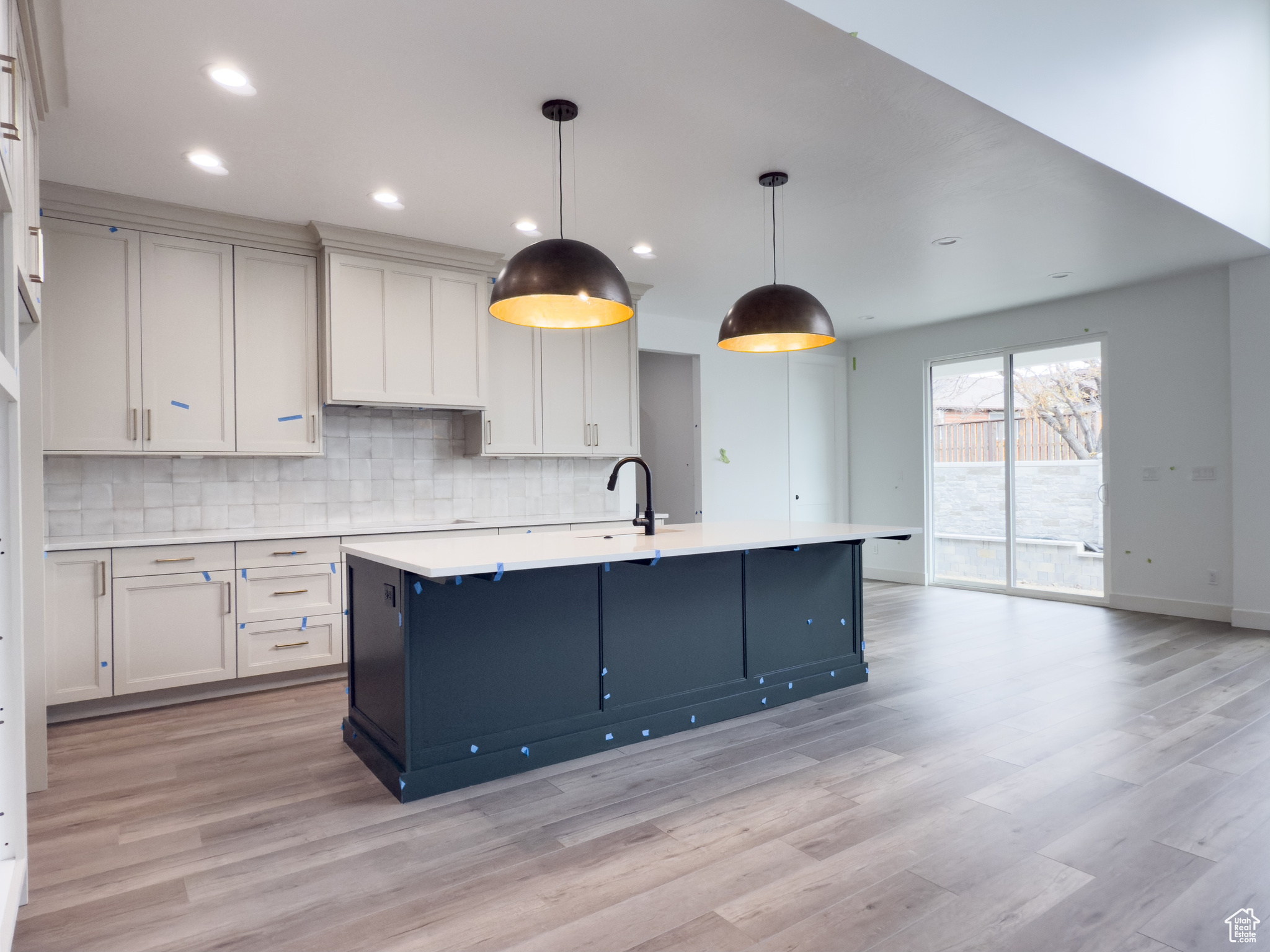 Kitchen with tasteful backsplash, decorative light fixtures, white cabinetry, and a kitchen island with sink