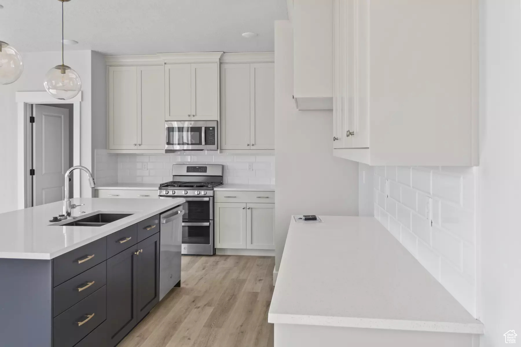 Kitchen featuring decorative light fixtures, stainless steel appliances, white cabinetry, and sink