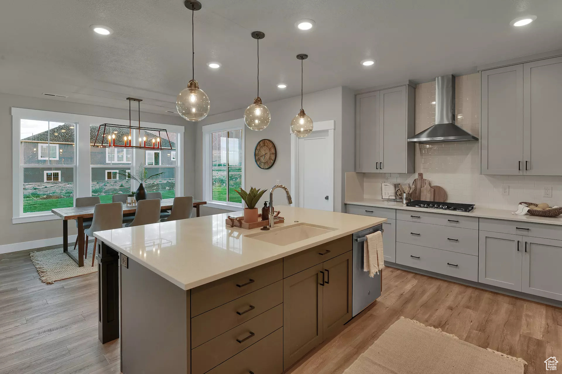 Kitchen with sink, stainless steel appliances, wall chimney range hood, light hardwood / wood-style flooring, and pendant lighting