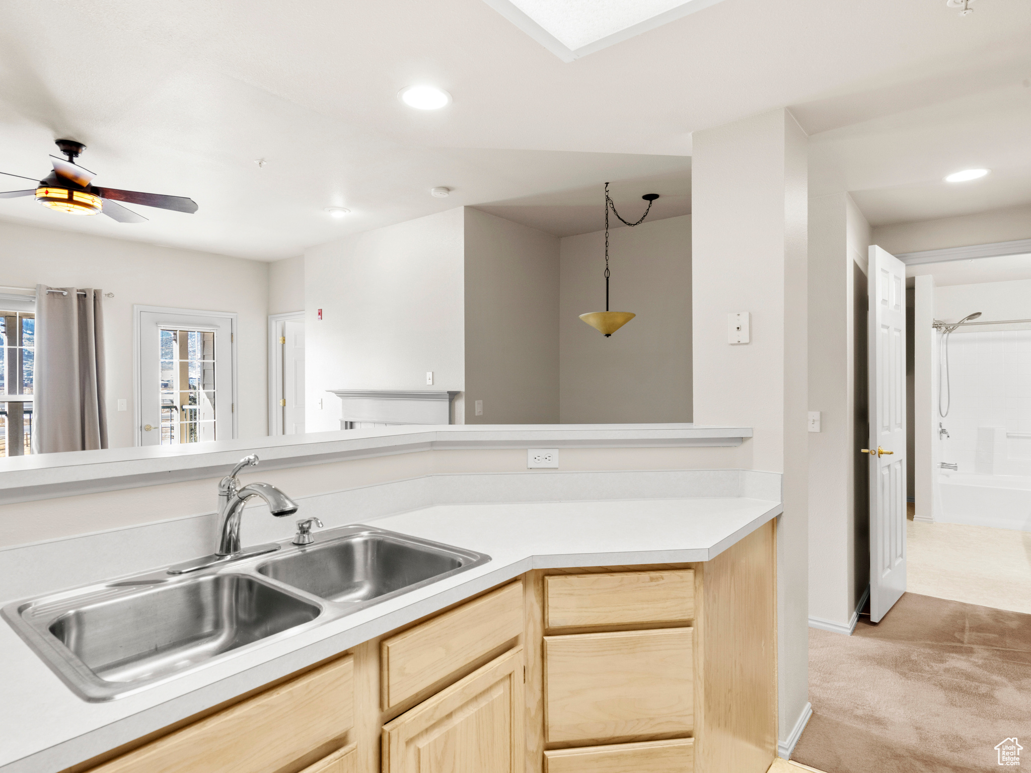 Kitchen featuring ceiling fan, sink, hanging light fixtures, light carpet, and light brown cabinetry