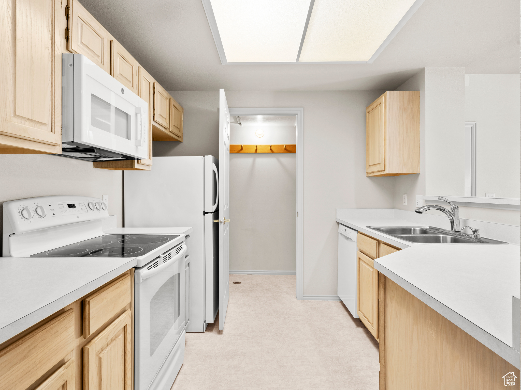 Kitchen with white appliances, sink, and light brown cabinetry