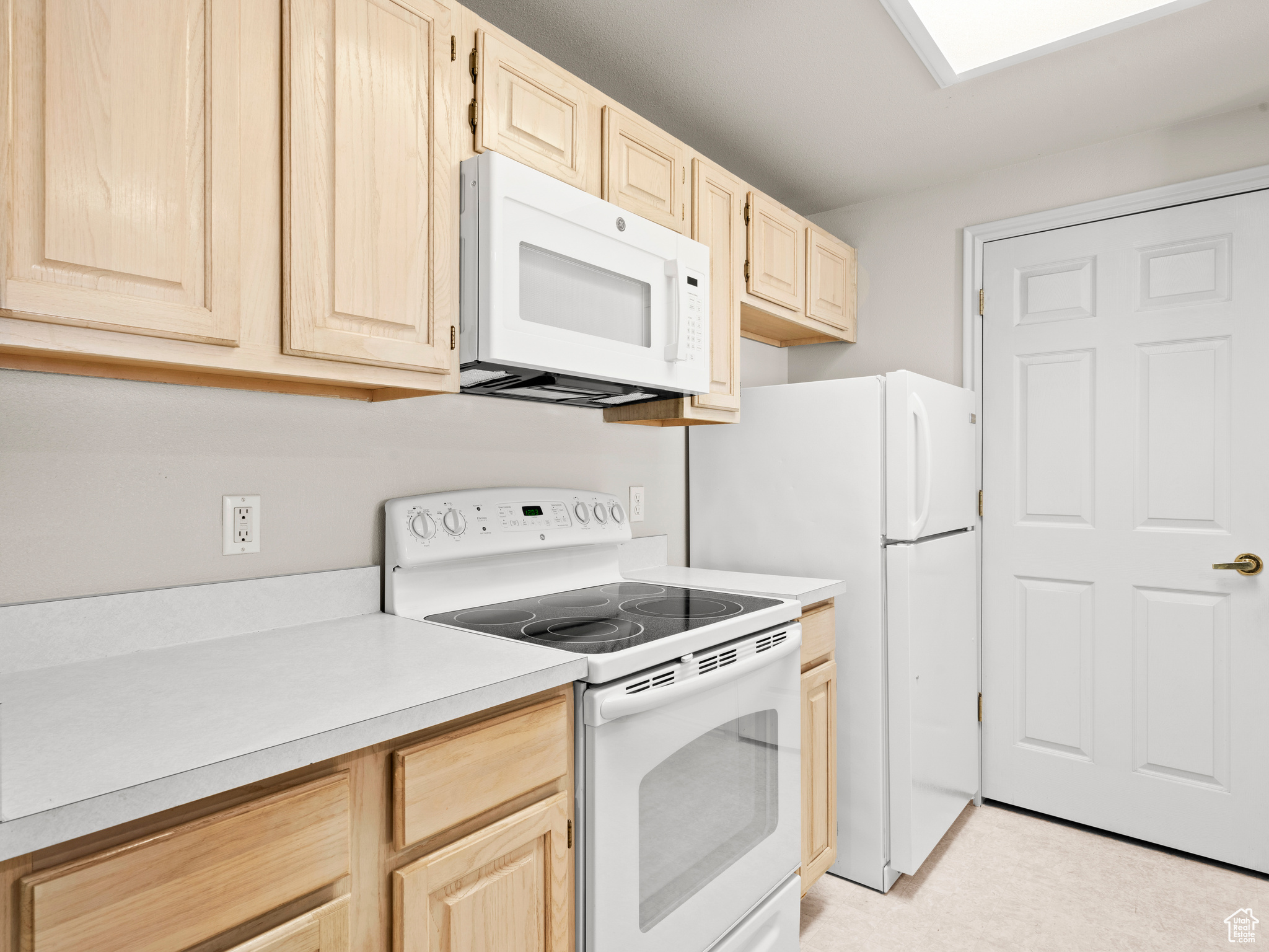 Kitchen with light brown cabinets and white appliances