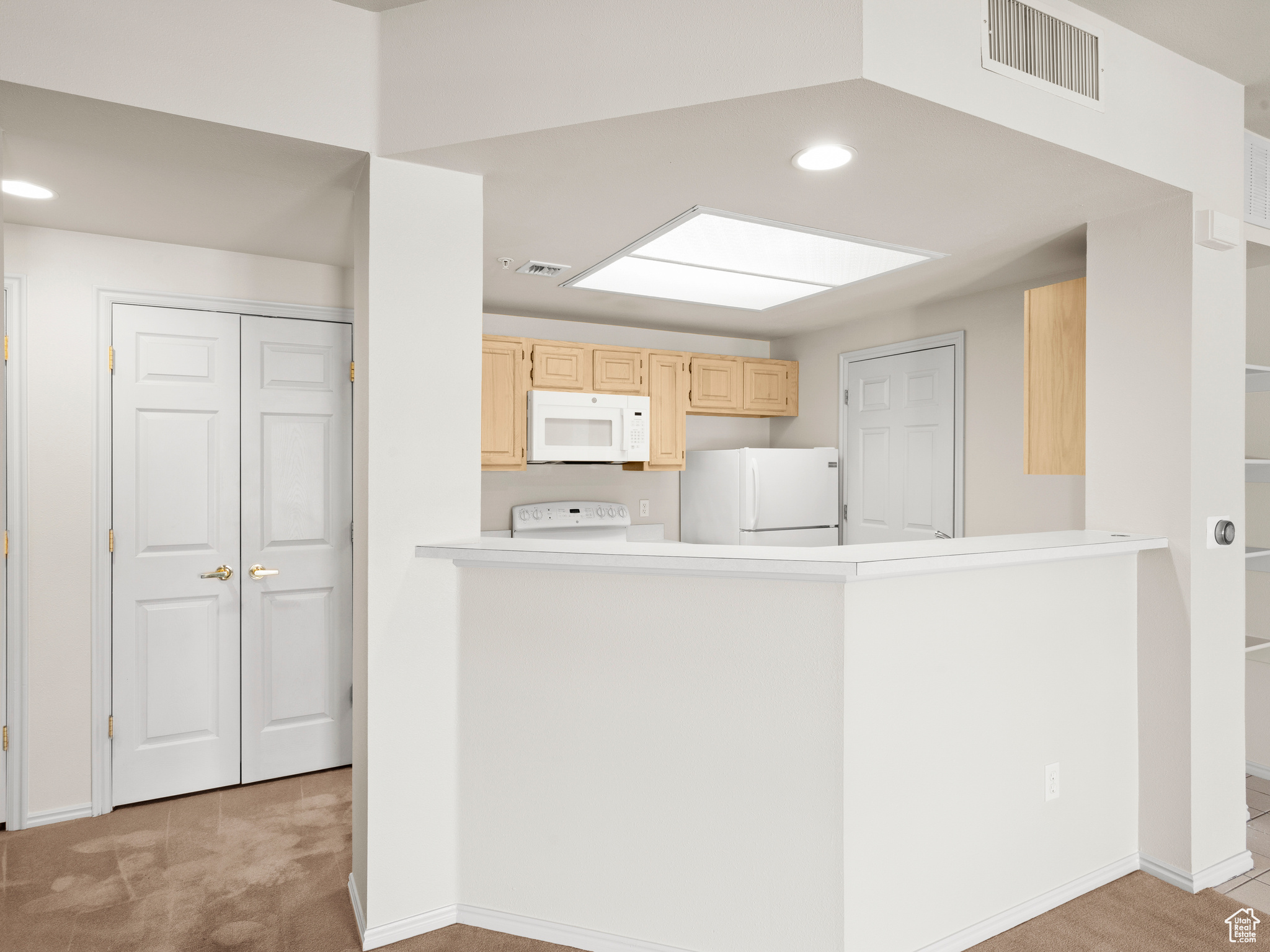 Kitchen featuring light colored carpet, white appliances, kitchen peninsula, and light brown cabinetry