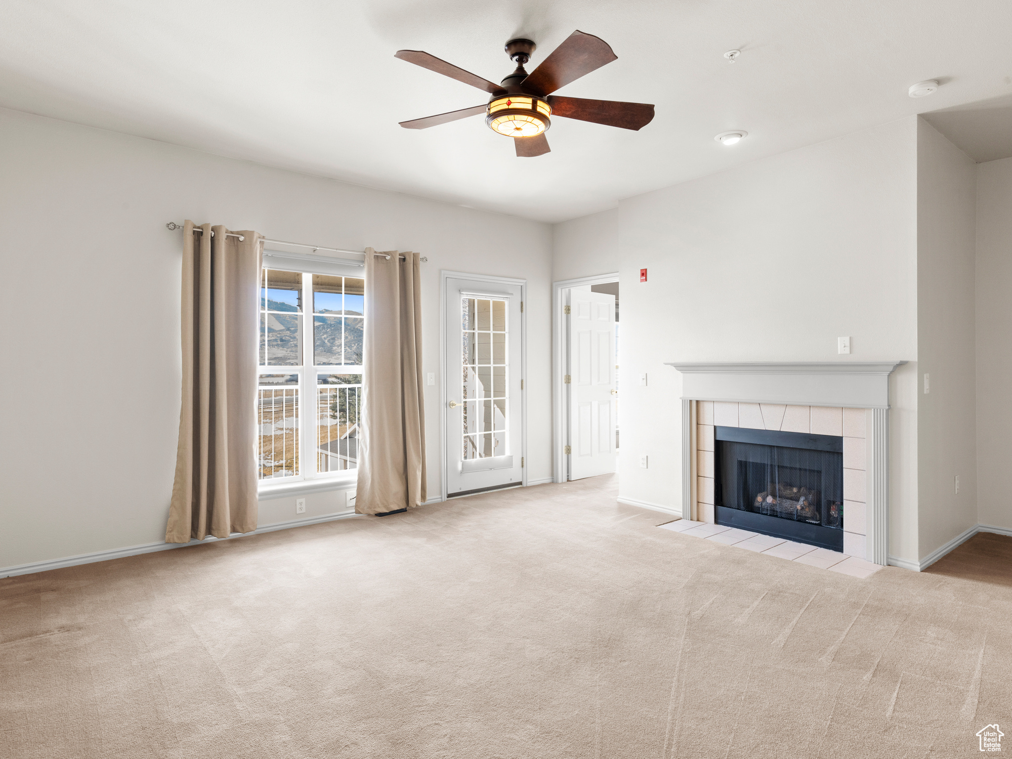 Unfurnished living room featuring light carpet, ceiling fan, and a tiled fireplace