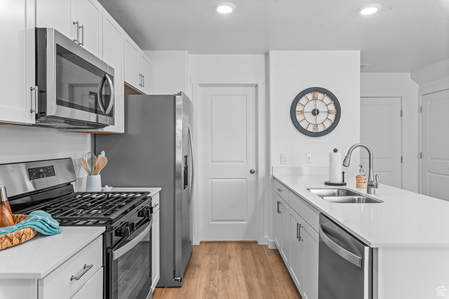 Kitchen with white cabinetry, sink, stainless steel appliances, kitchen peninsula, and light hardwood / wood-style floors