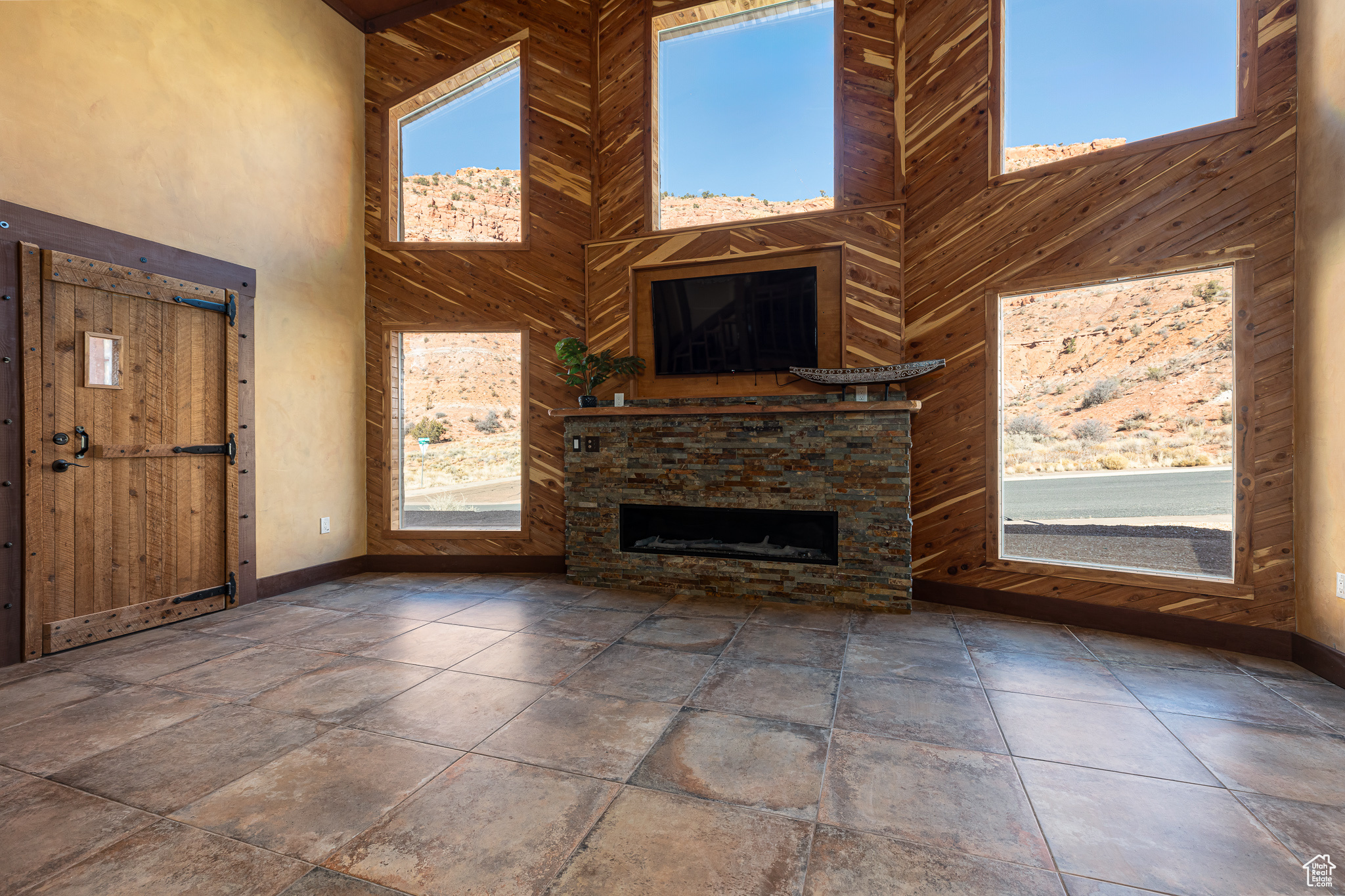 Unfurnished living room with wooden walls, an outdoor stone fireplace, and high vaulted ceiling