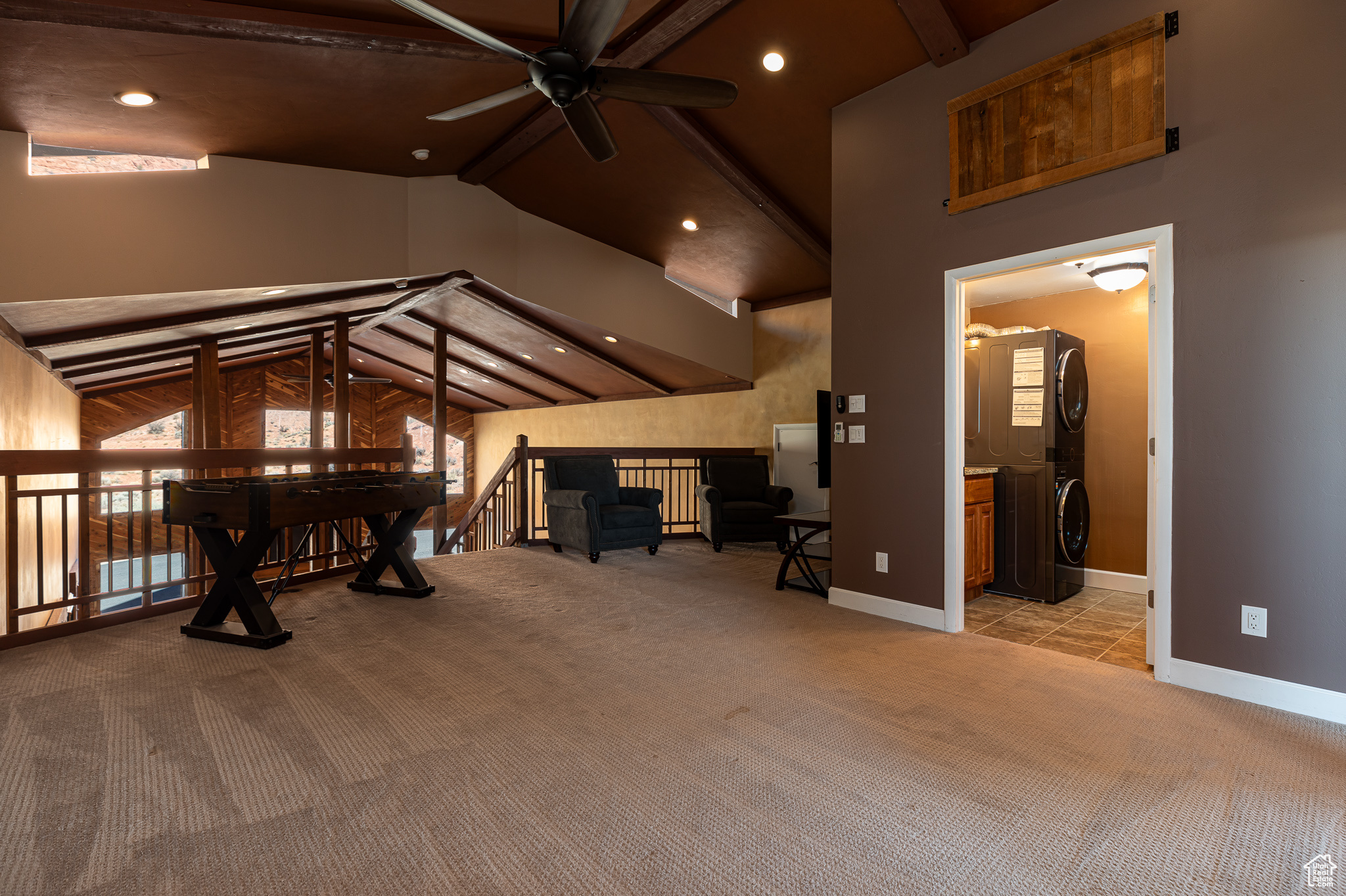 Family Room featuring vaulted ceiling with beams, light carpet, ensuite bathroom, and stacked washer and clothes dryer