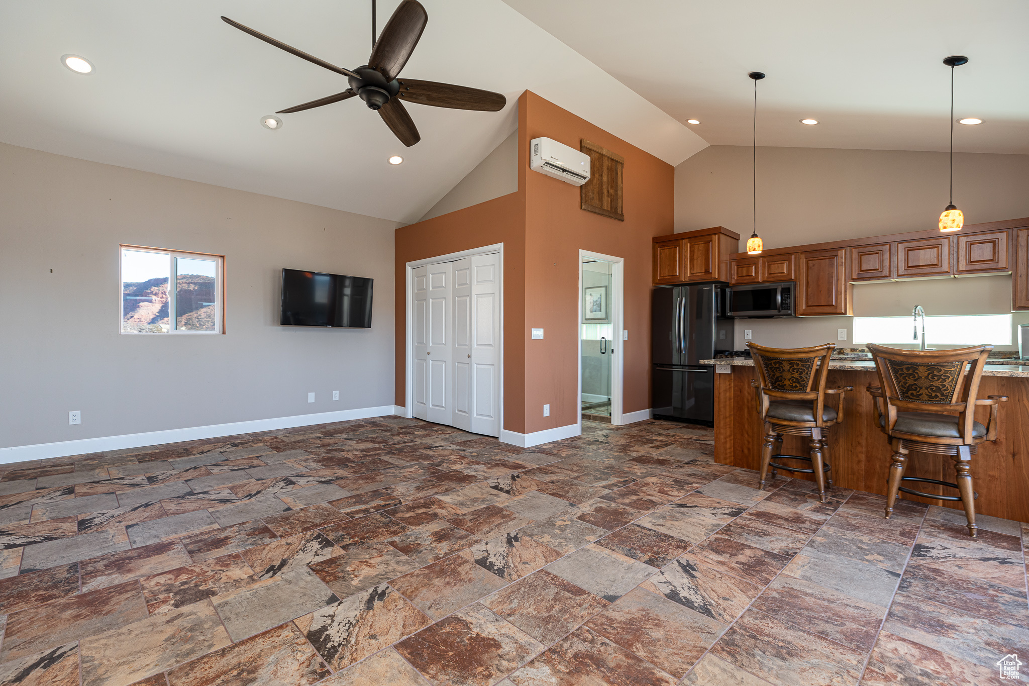 Studio Kitchen featuring black refrigerator, an AC wall unit, a breakfast bar area, and high vaulted ceiling