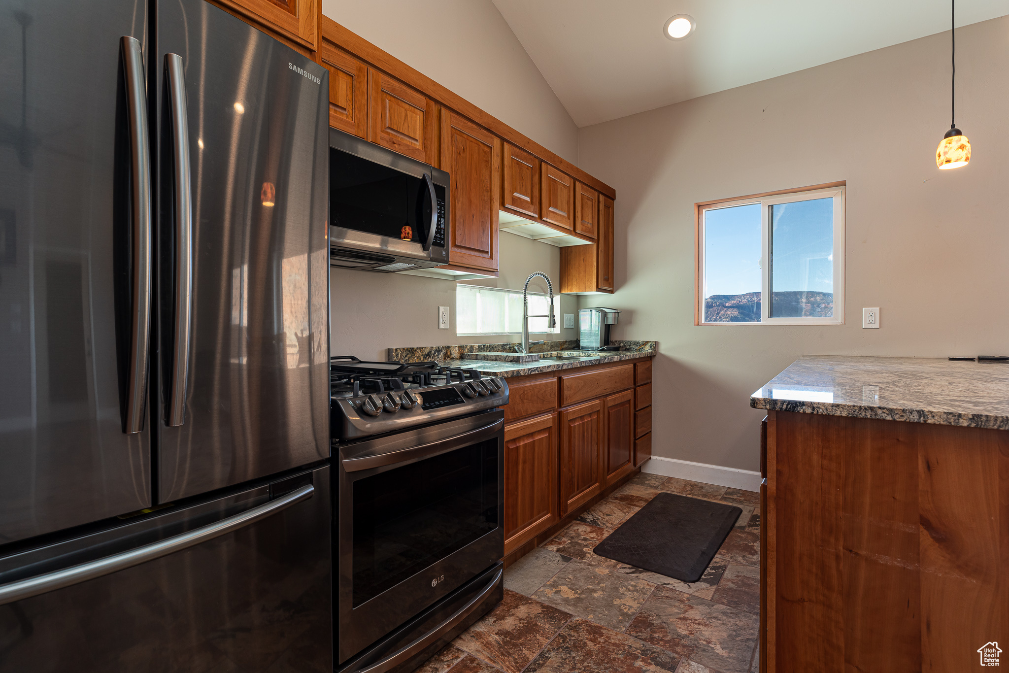 Kitchen featuring lofted ceiling, sink, hanging light fixtures, light stone countertops, and stainless steel appliances