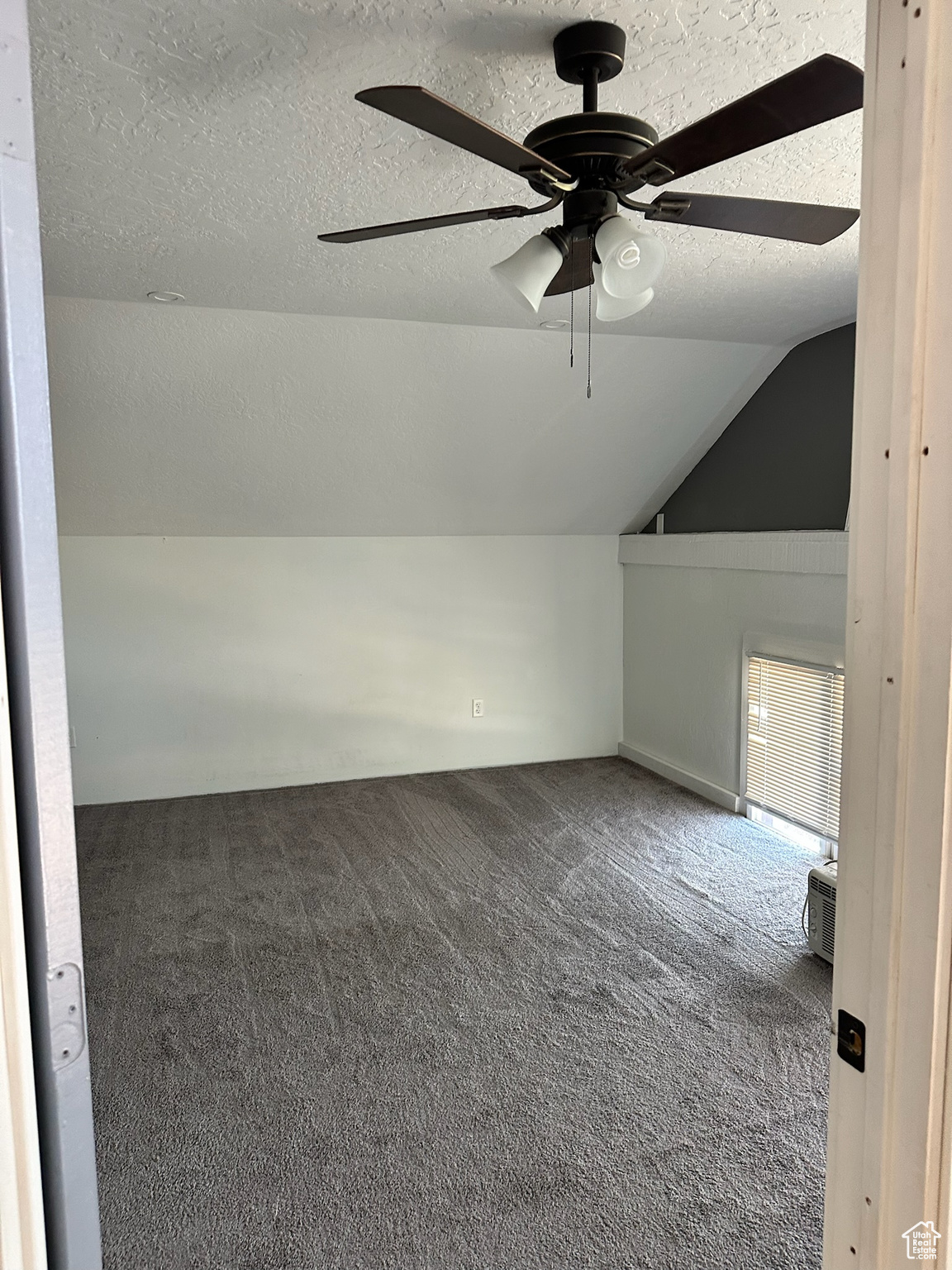 Bonus room with dark colored carpet, a textured ceiling, vaulted ceiling, and ceiling fan