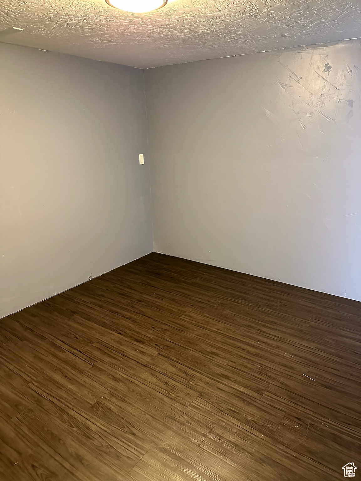 Empty room featuring a textured ceiling and dark wood-type flooring