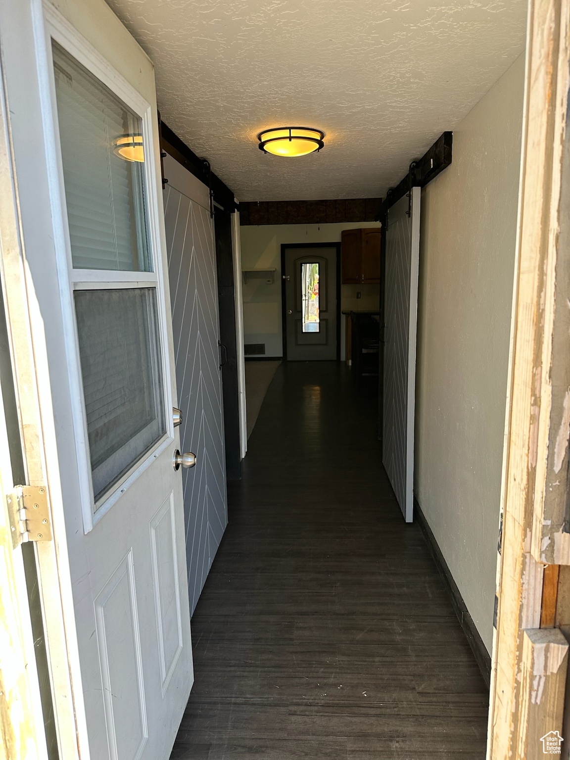 Hallway with a barn door, dark wood-type flooring, and a textured ceiling