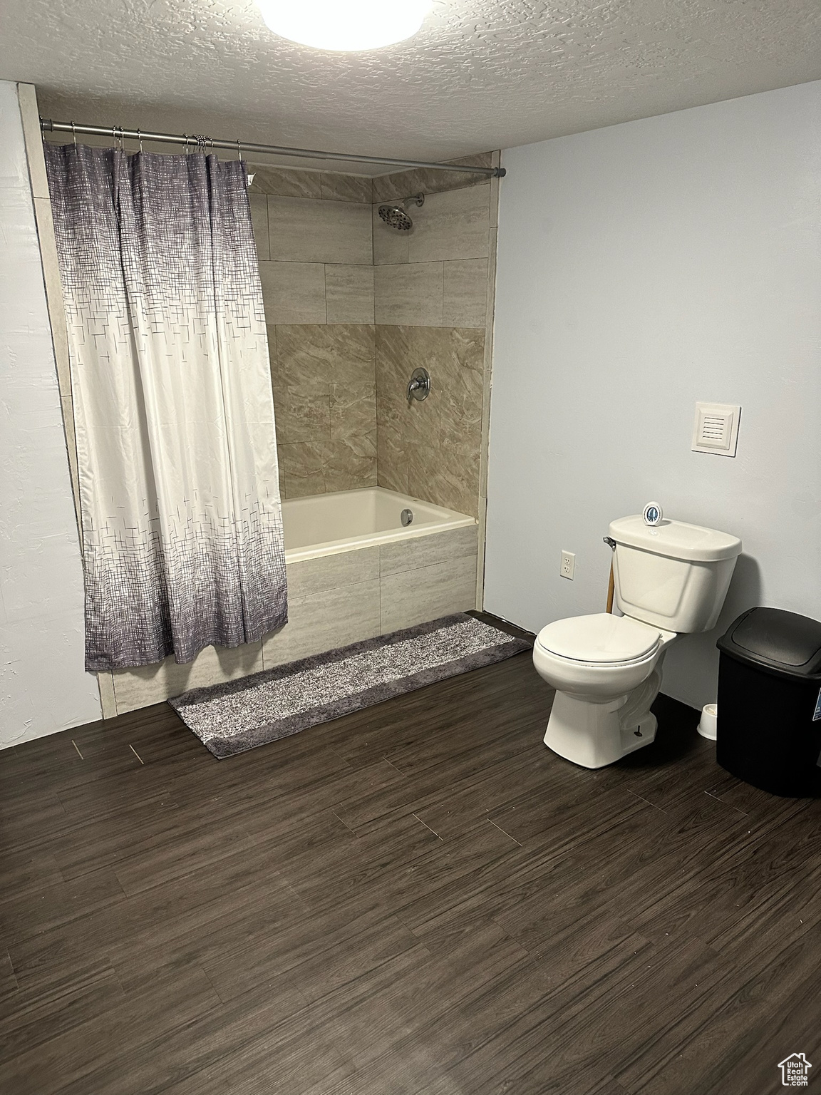 Bathroom with a textured ceiling, toilet, and shower / bath combo with shower curtain