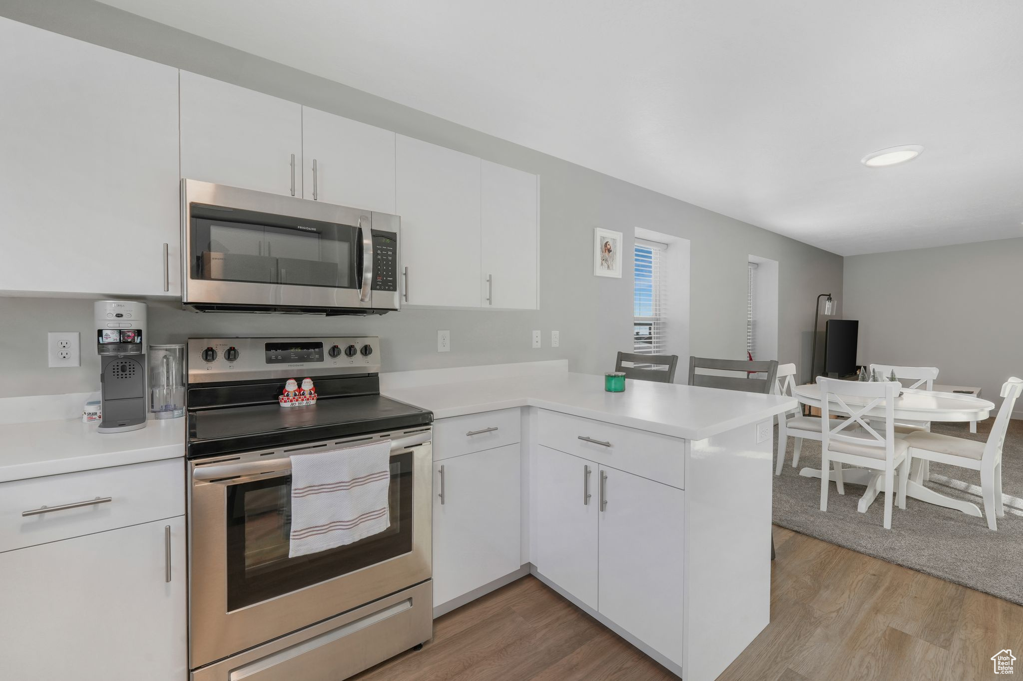 Kitchen with white cabinets, light hardwood / wood-style floors, kitchen peninsula, and appliances with stainless steel finishes