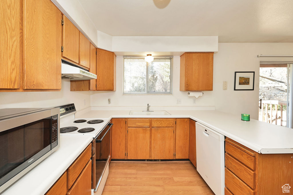 Kitchen with light wood-type flooring, white appliances, kitchen peninsula, and sink