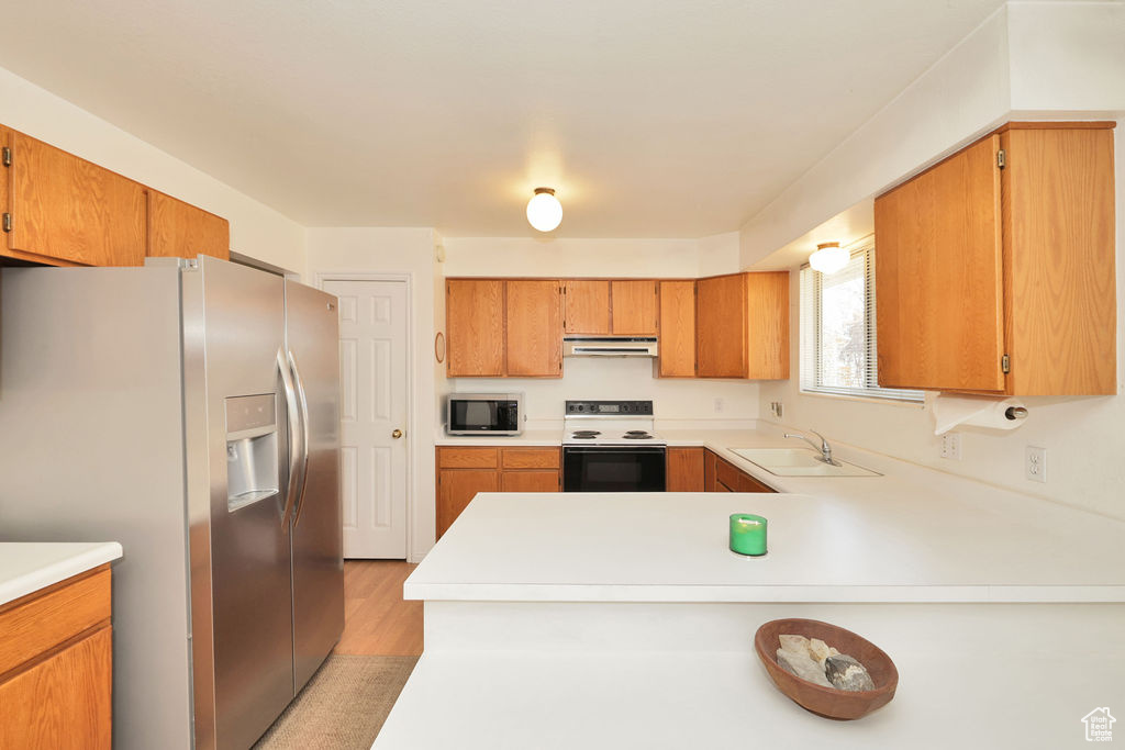 Kitchen featuring white range with electric cooktop, sink, stainless steel refrigerator with ice dispenser, light hardwood / wood-style floors, and kitchen peninsula