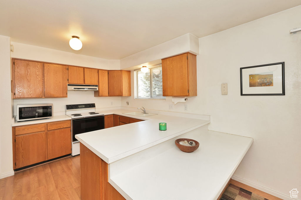 Kitchen featuring kitchen peninsula, white appliances, light hardwood / wood-style floors, and sink