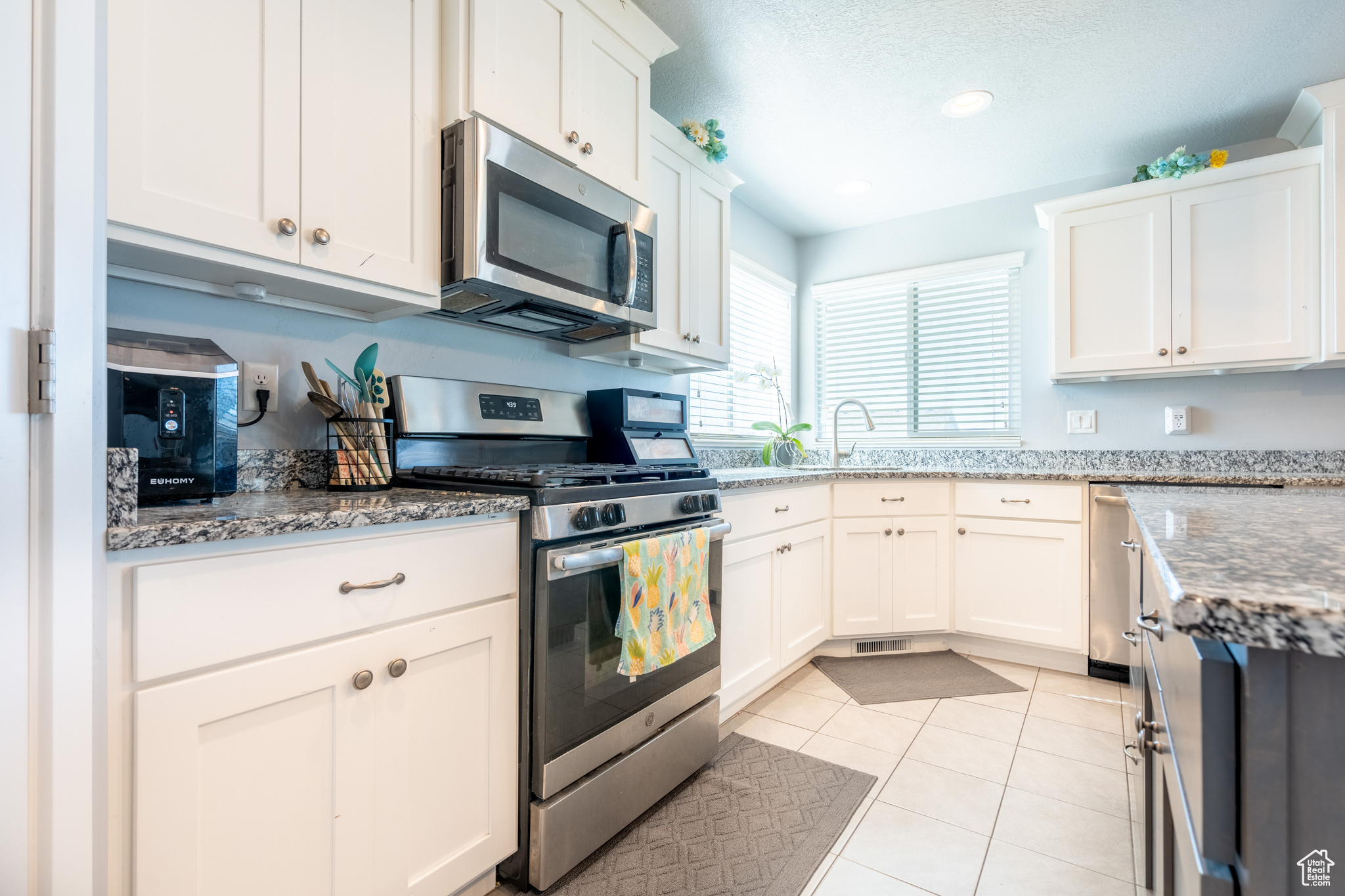 Kitchen featuring light stone countertops, a textured ceiling, stainless steel appliances, light tile patterned floors, and white cabinets