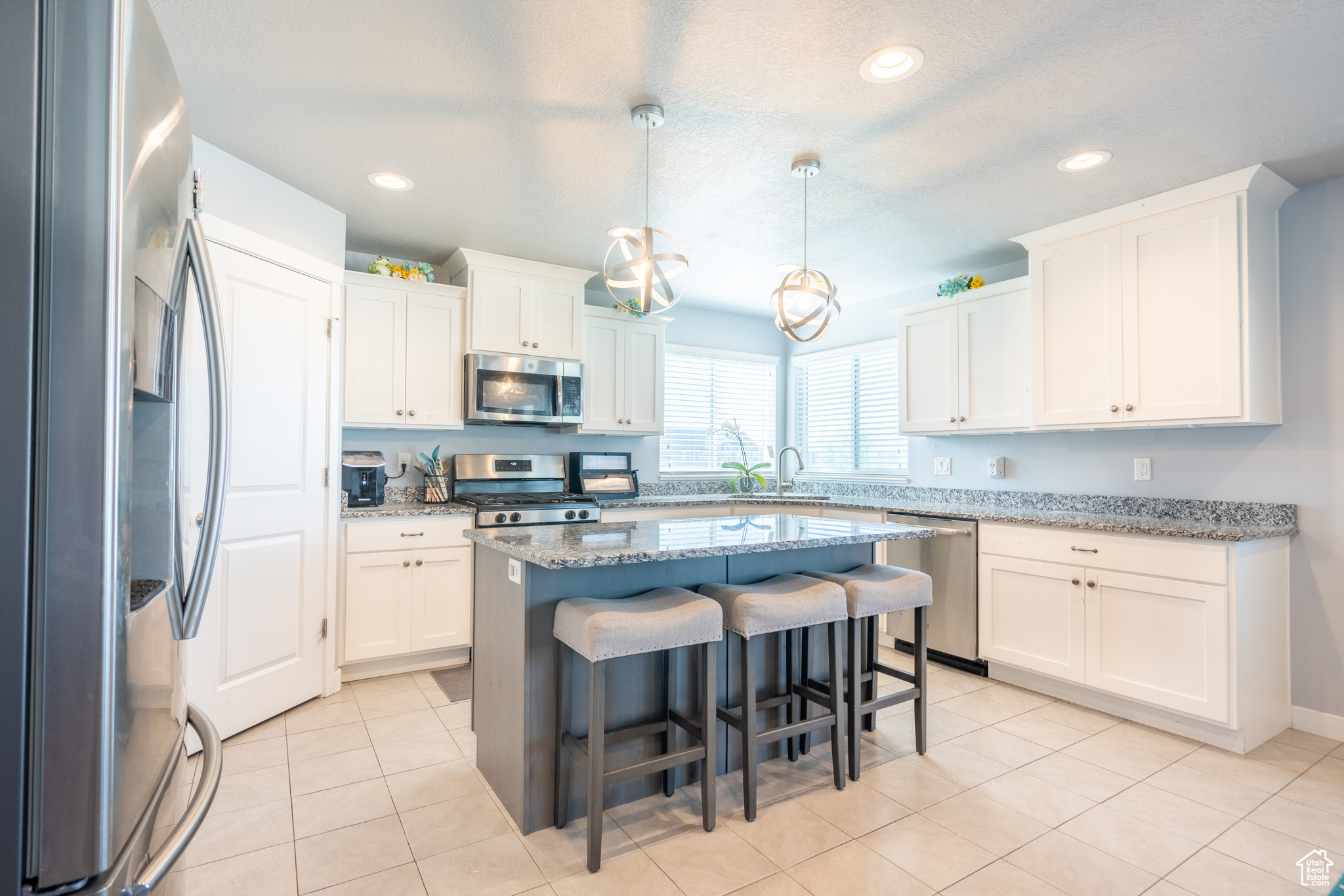 Kitchen with white cabinetry, light stone countertops, stainless steel appliances, decorative light fixtures, and a kitchen island