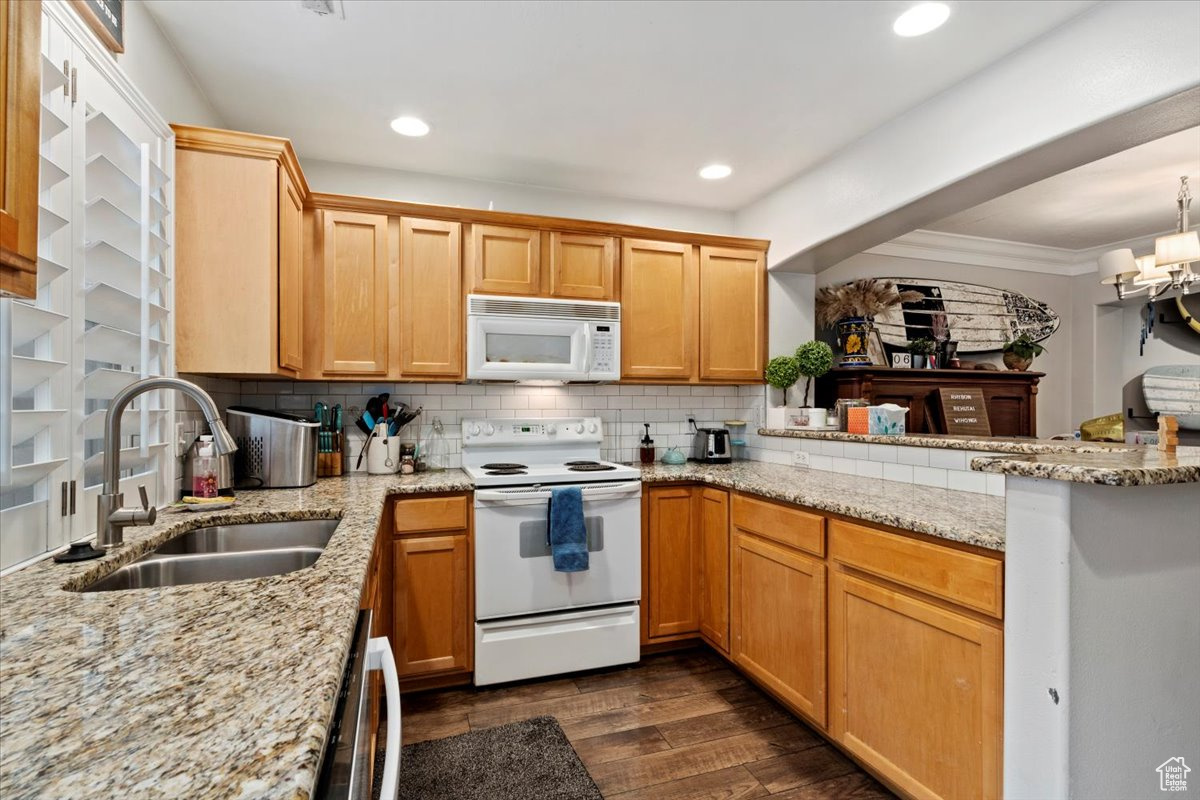 Kitchen featuring kitchen peninsula, decorative backsplash, white appliances, and sink