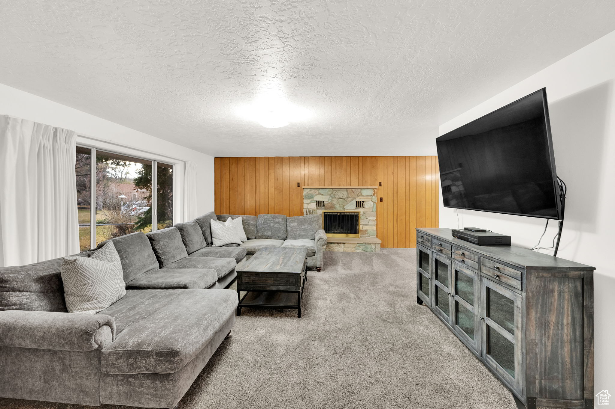 Carpeted living room featuring a textured ceiling, wood walls, and a fireplace