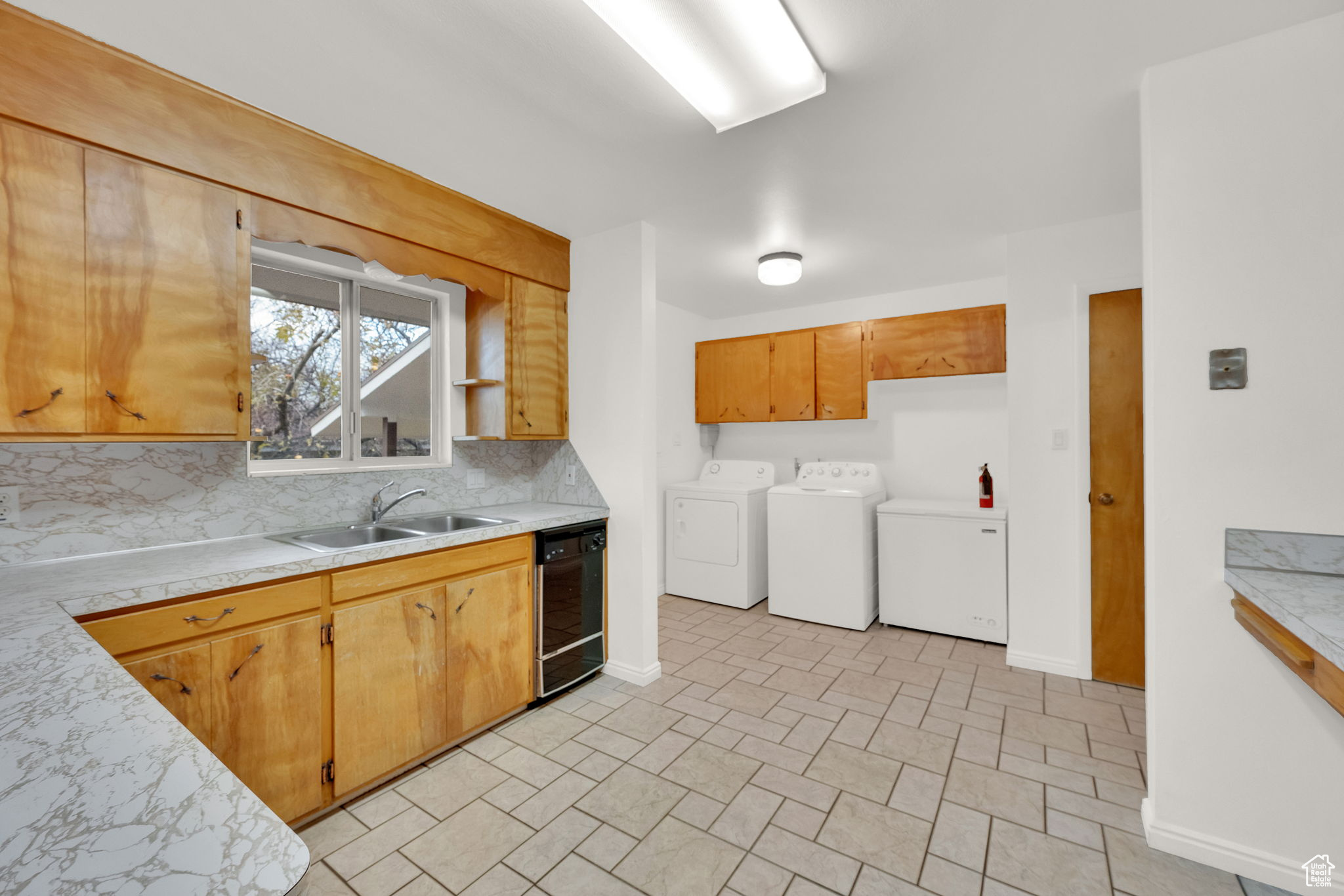 Kitchen featuring washer and clothes dryer, dishwasher, sink, and tasteful backsplash