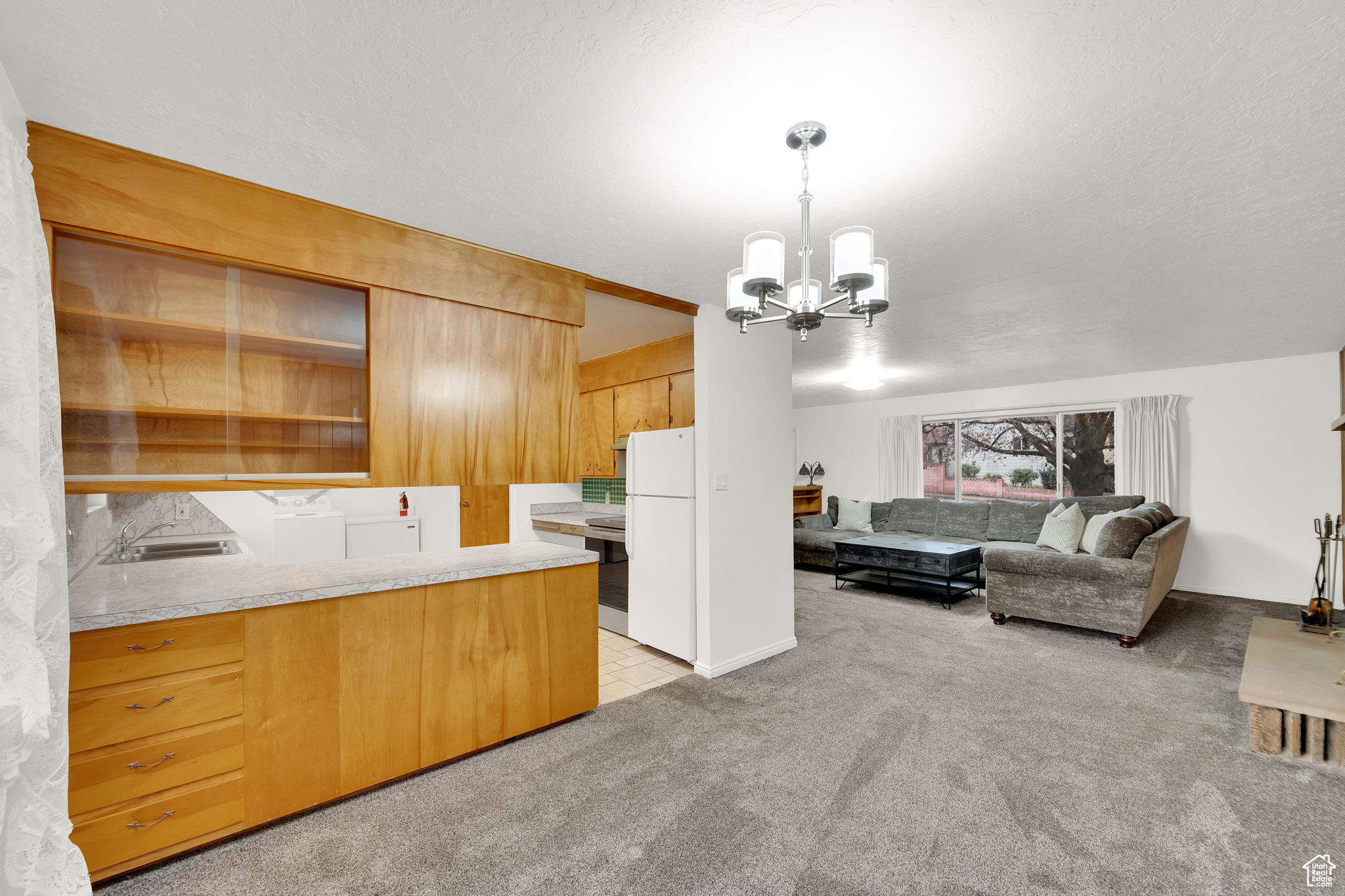 Kitchen featuring hanging light fixtures, a notable chandelier, kitchen peninsula, white fridge, and light carpet