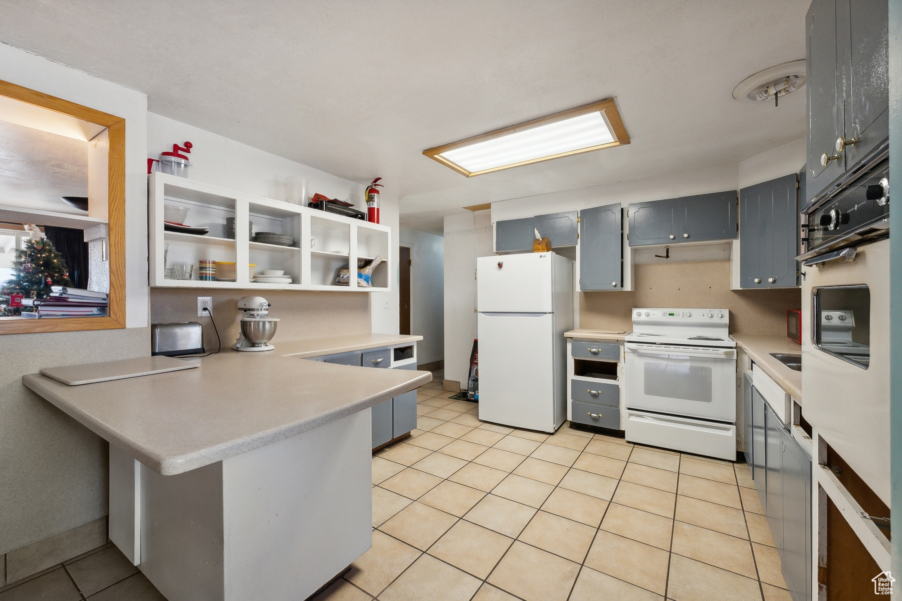 Kitchen featuring kitchen peninsula, white appliances, gray cabinets, and light tile patterned flooring