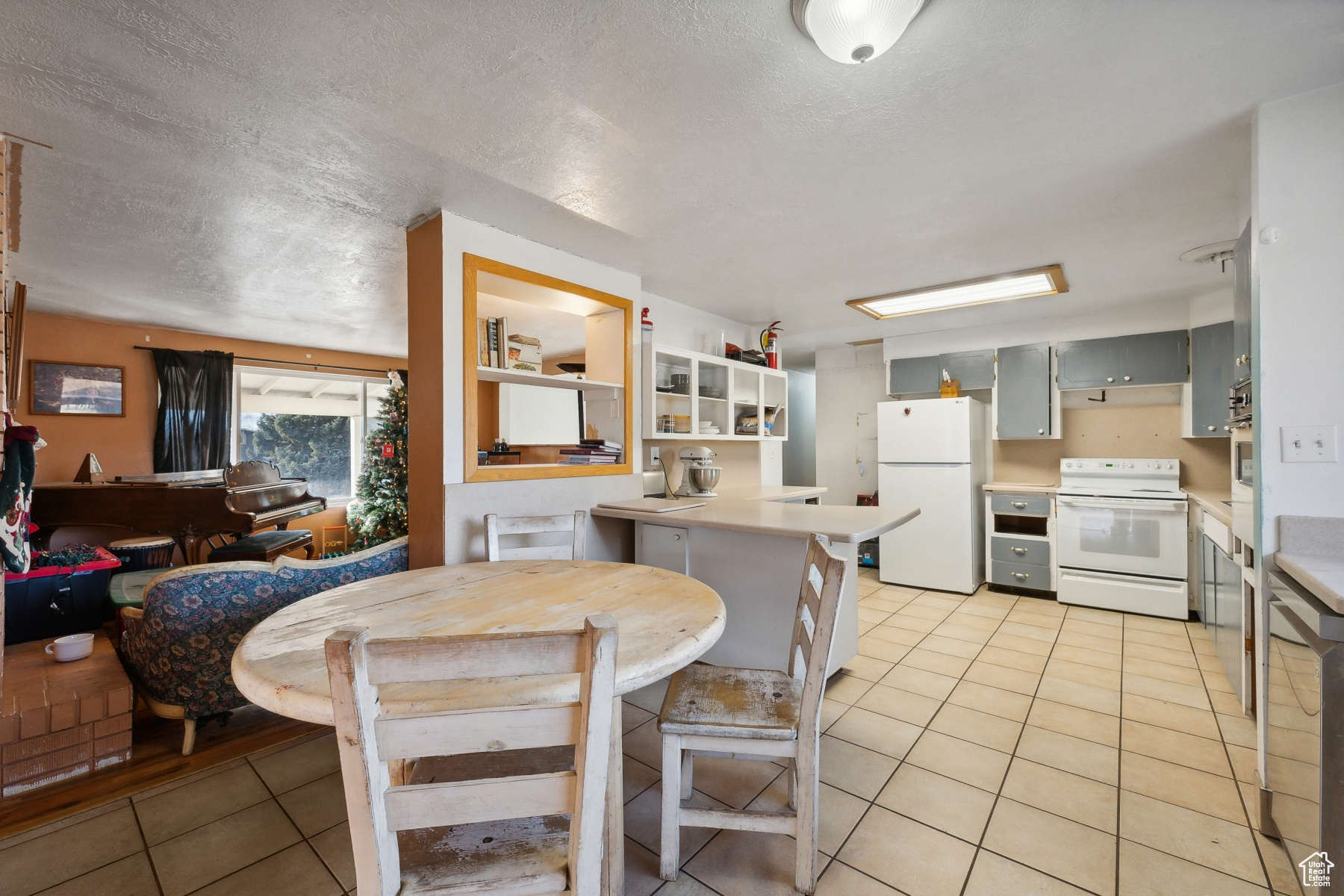 Kitchen featuring a kitchen bar, white appliances, gray cabinets, and light tile patterned flooring