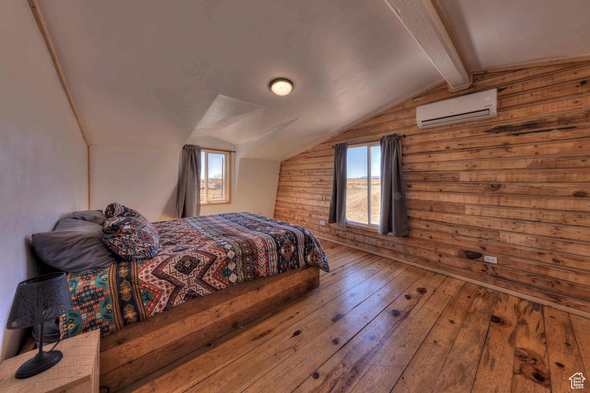 Bedroom featuring a wall mounted AC, lofted ceiling with beams, wood-type flooring, and multiple windows